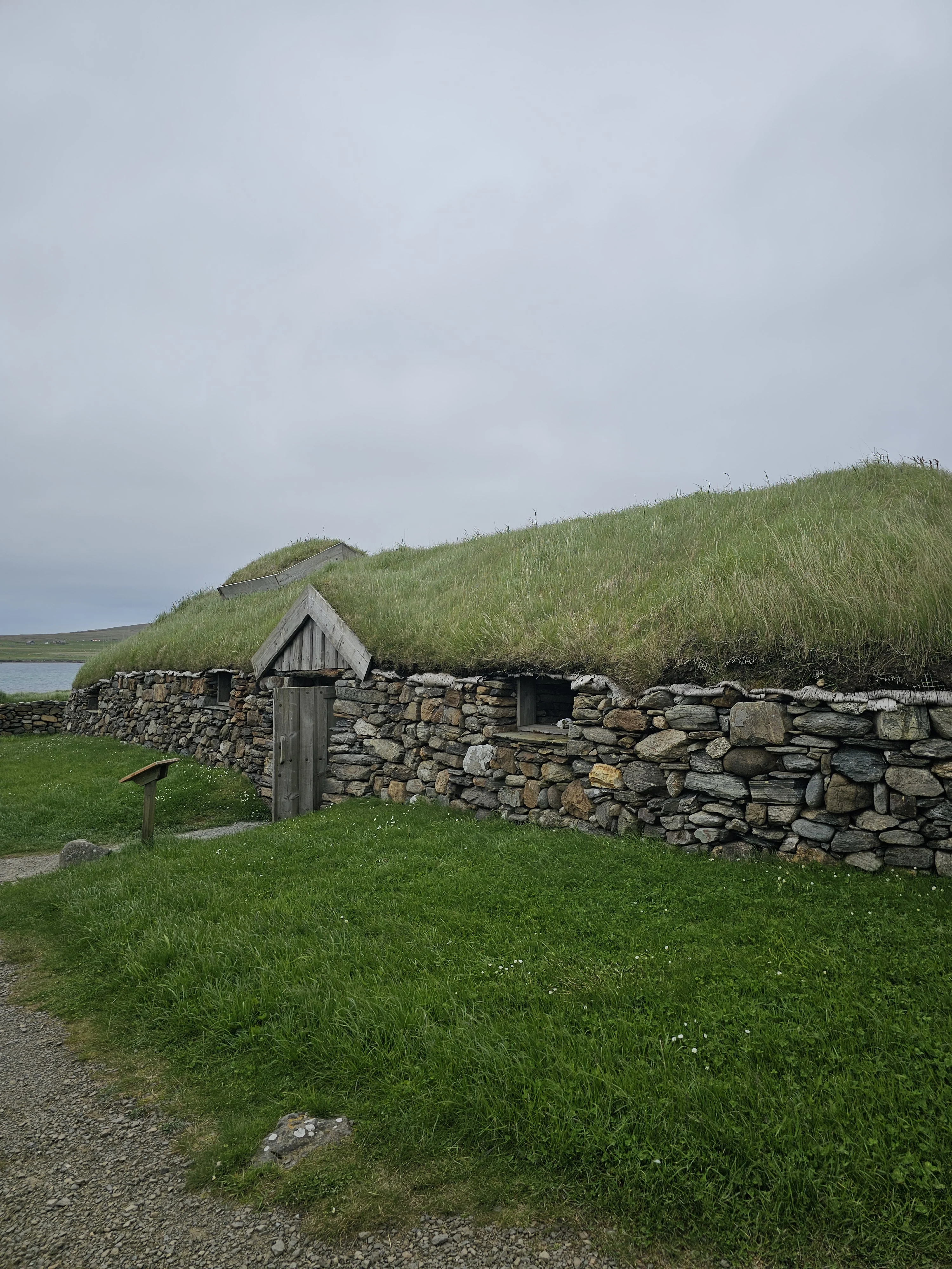 Historic Scottish turf-roofed stone cottage with grassy hillside and water beyond
