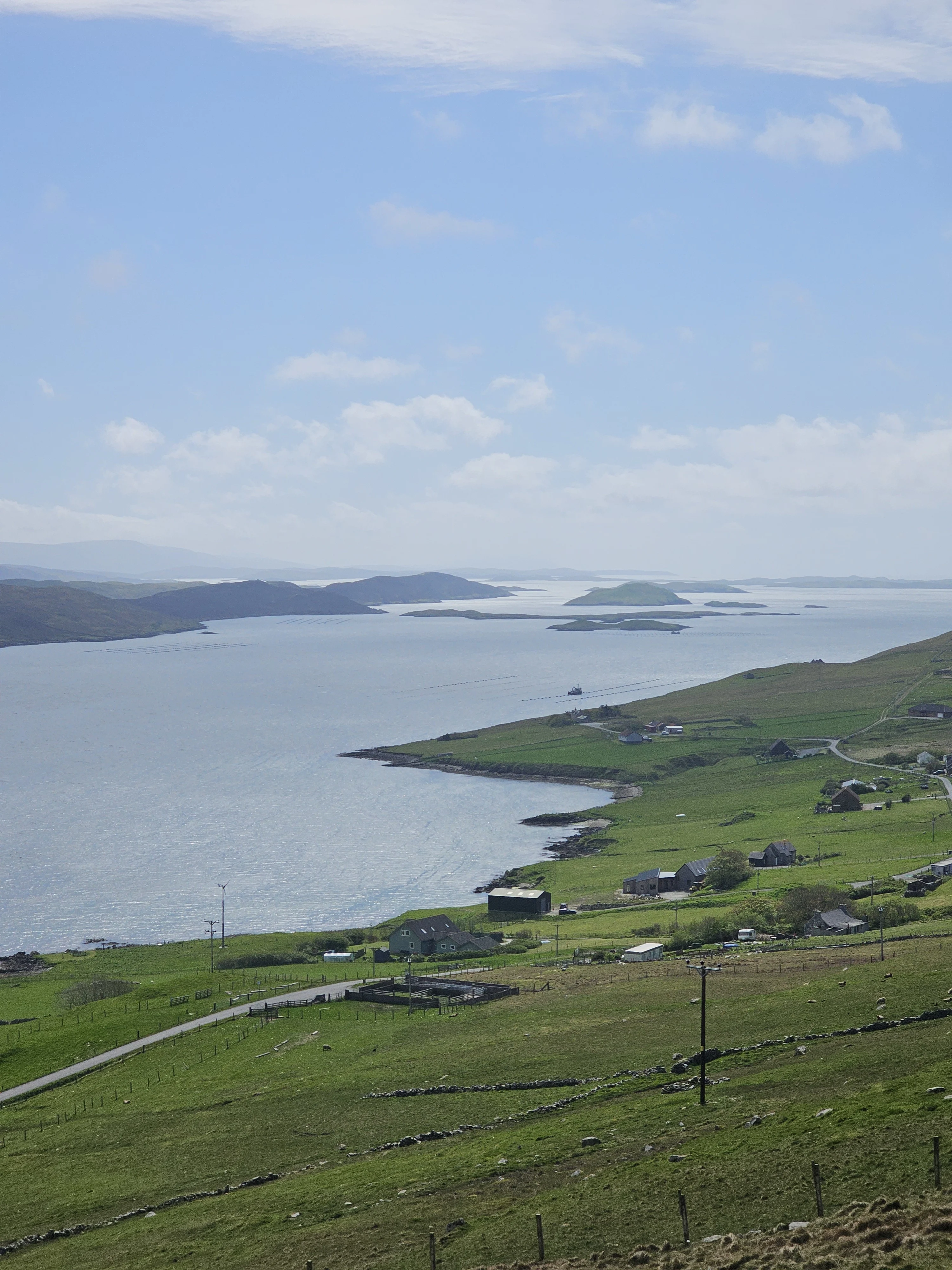 Scenic Scottish coastal landscape with green hillside, scattered houses, and islands in blue water.