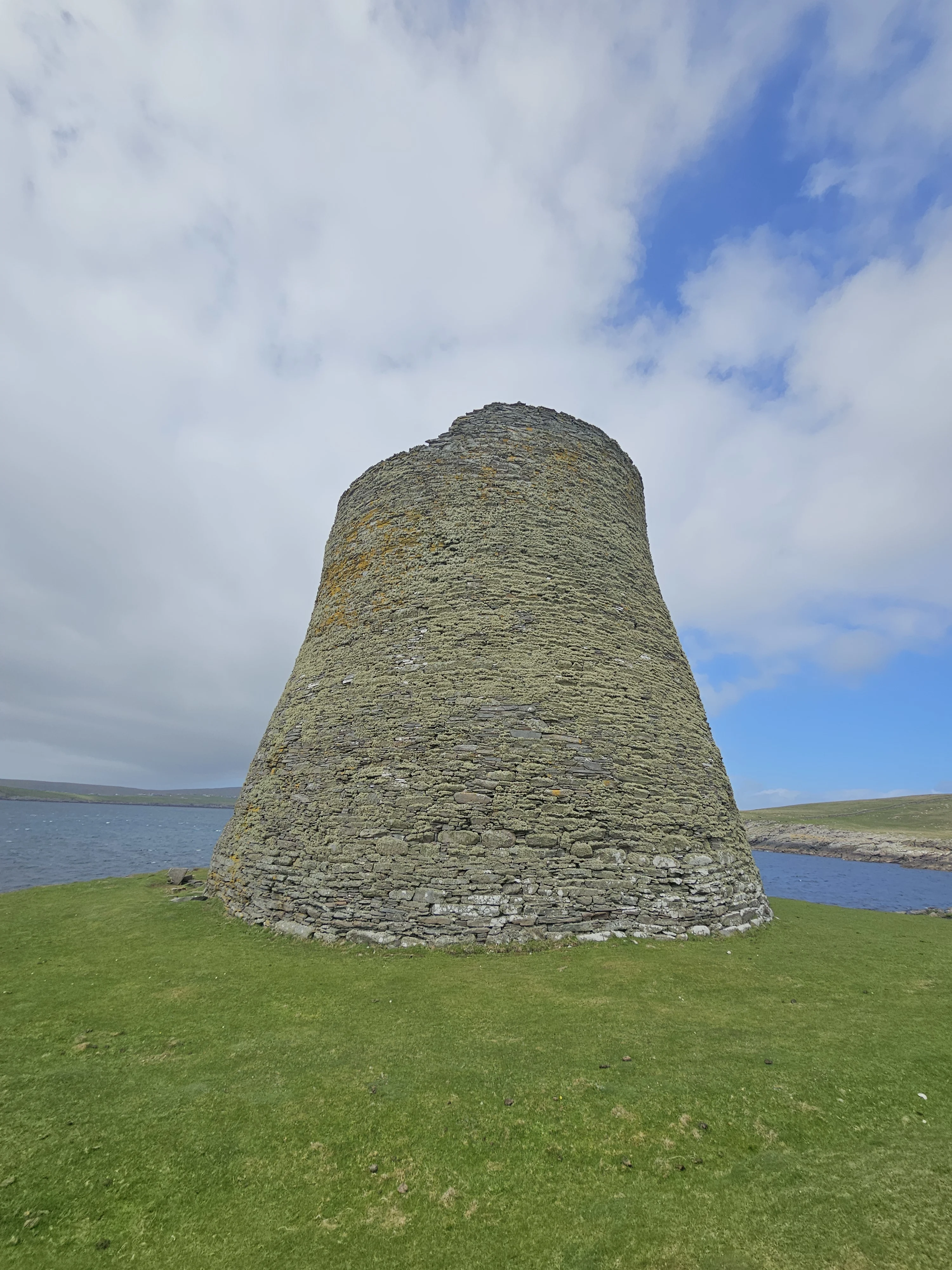 Ancient stone broch tower standing on green grass by Scottish waters
