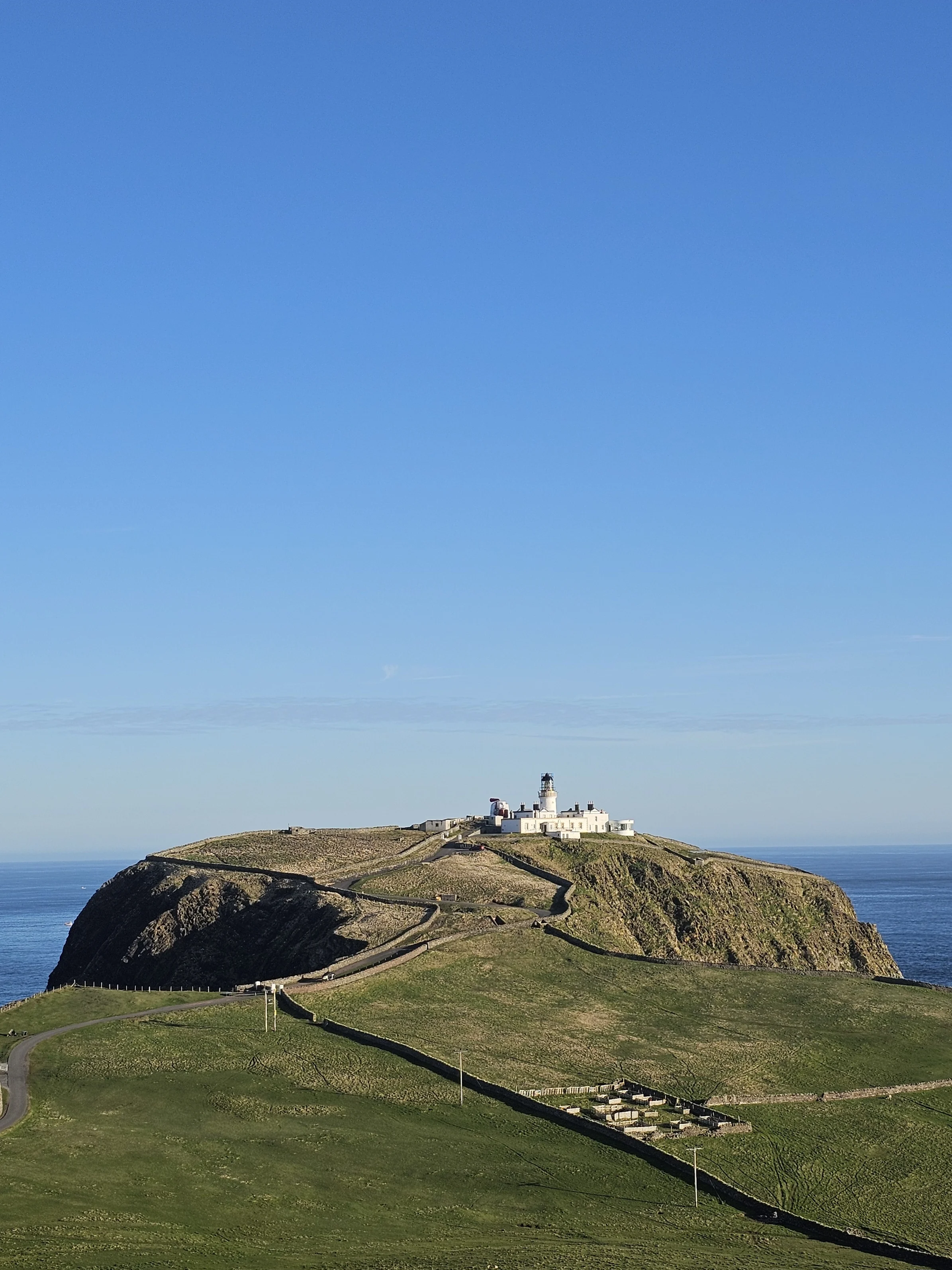 Lighthouse on rocky headland overlooking Scottish coastline under blue sky