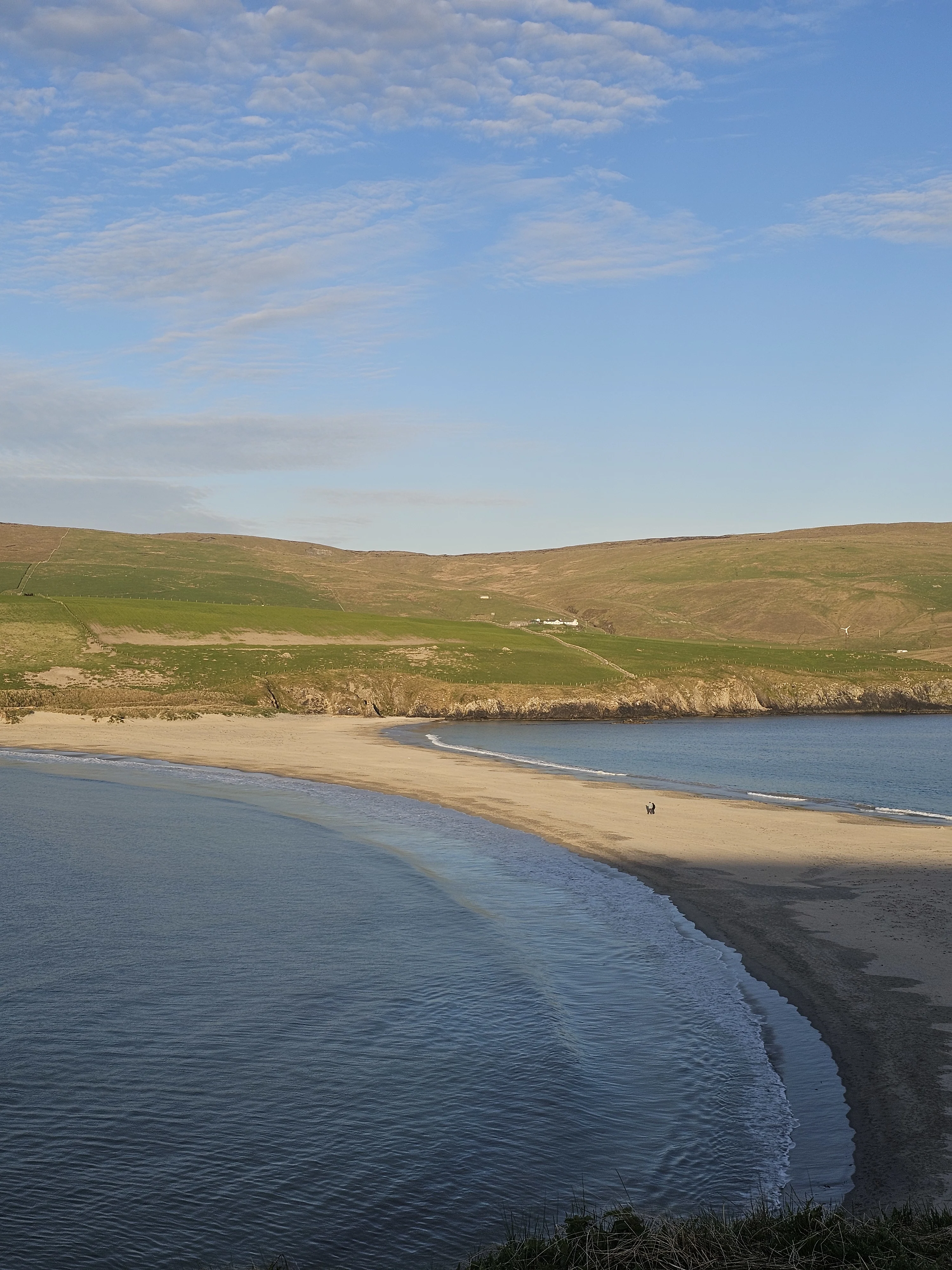 Scenic Scottish beach with golden sand, rolling green hills, and blue sky