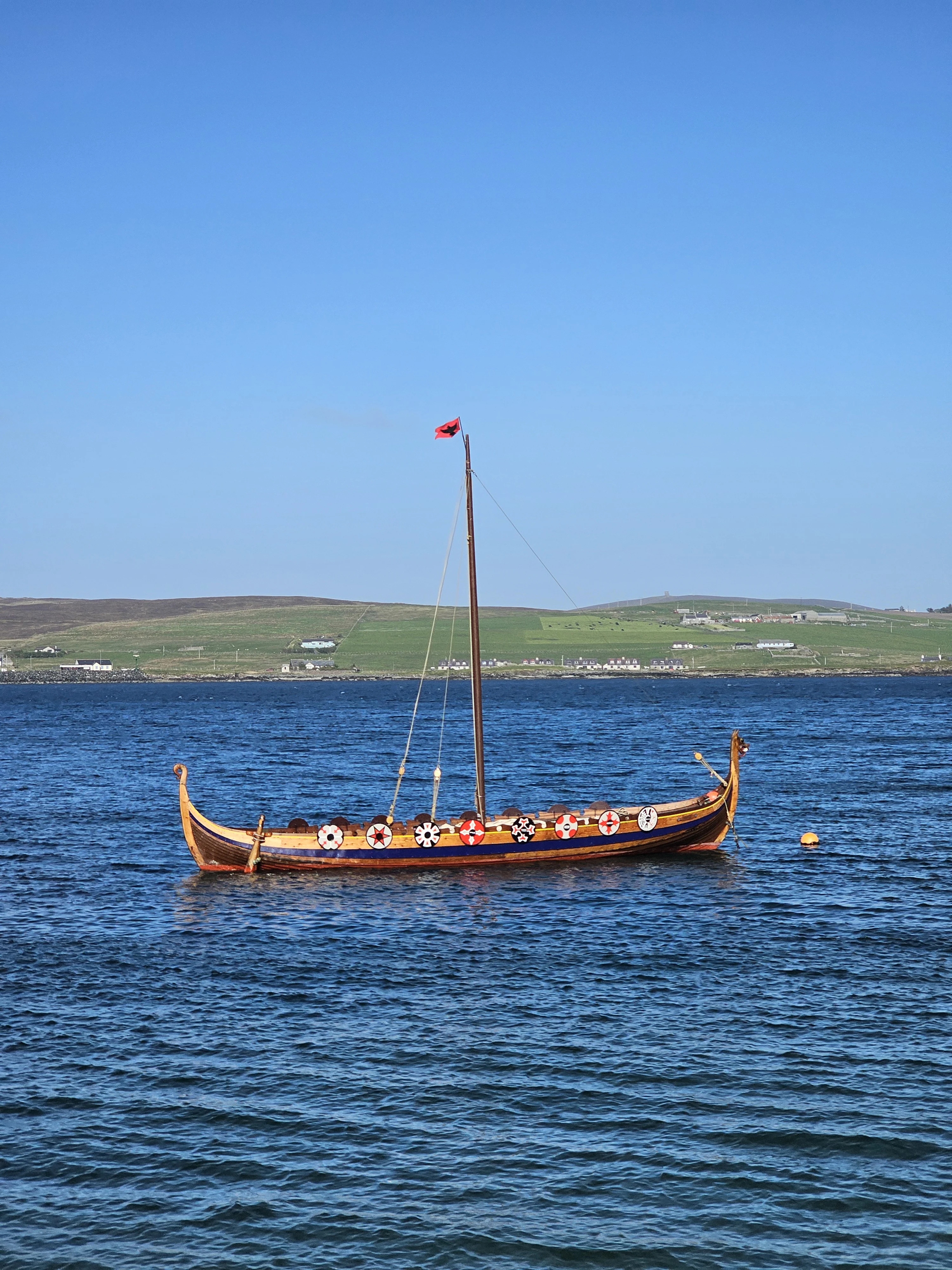 Traditional Viking longship moored in Scottish coastal waters with green hills beyond