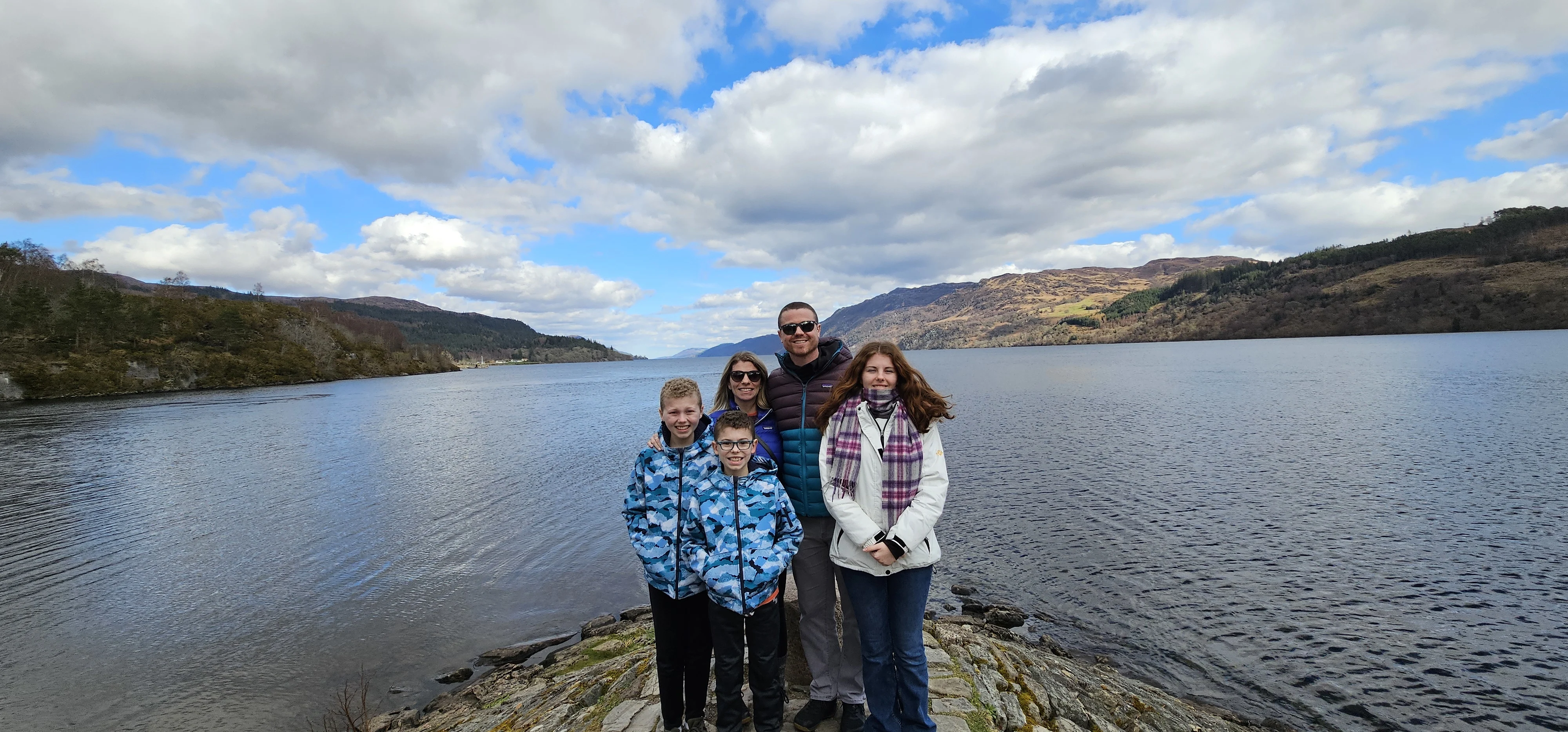 Family posing by Scottish loch with mountains and blue sky