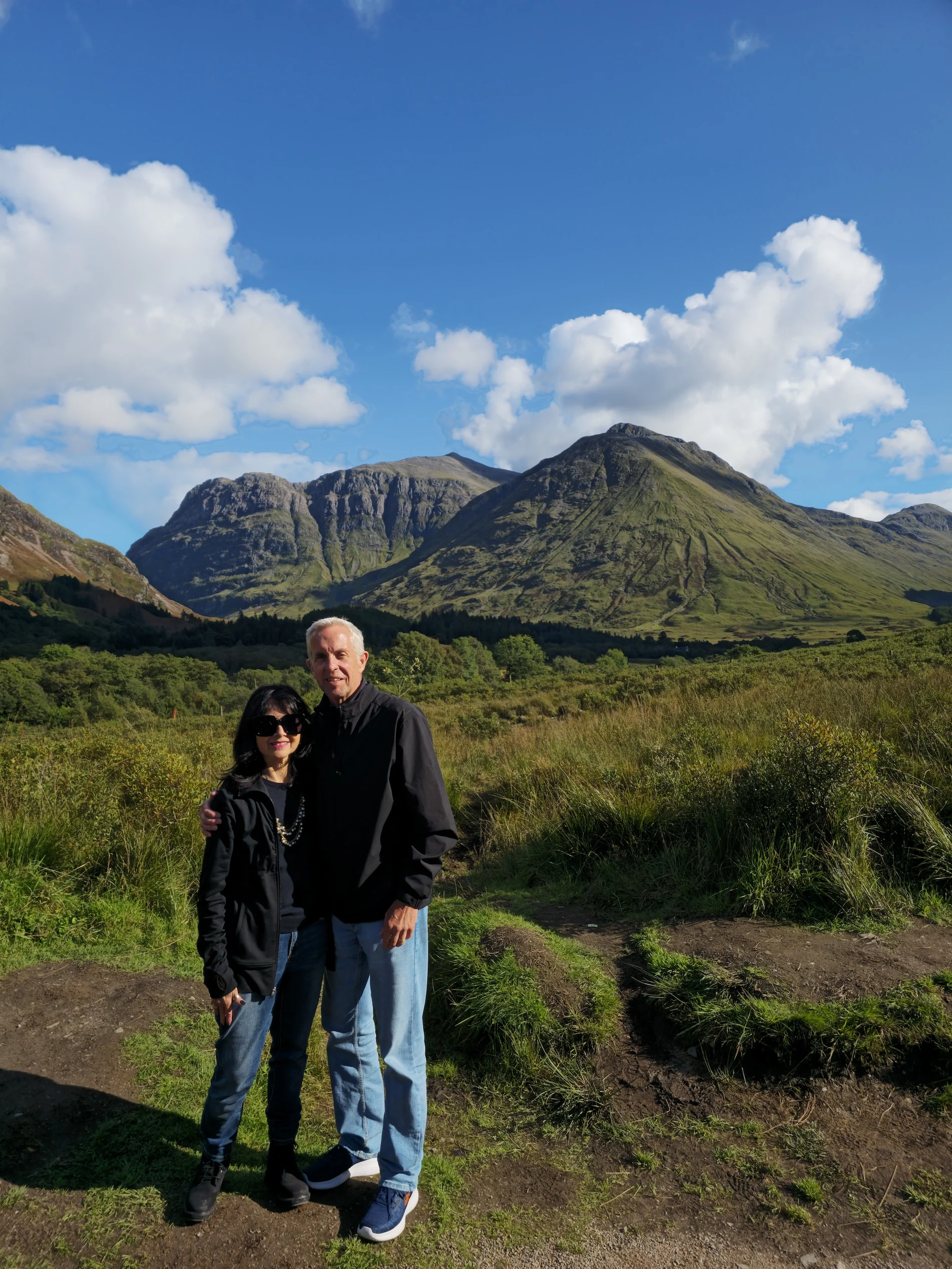 Couple posing in Scottish Highlands with dramatic mountain peaks behind them