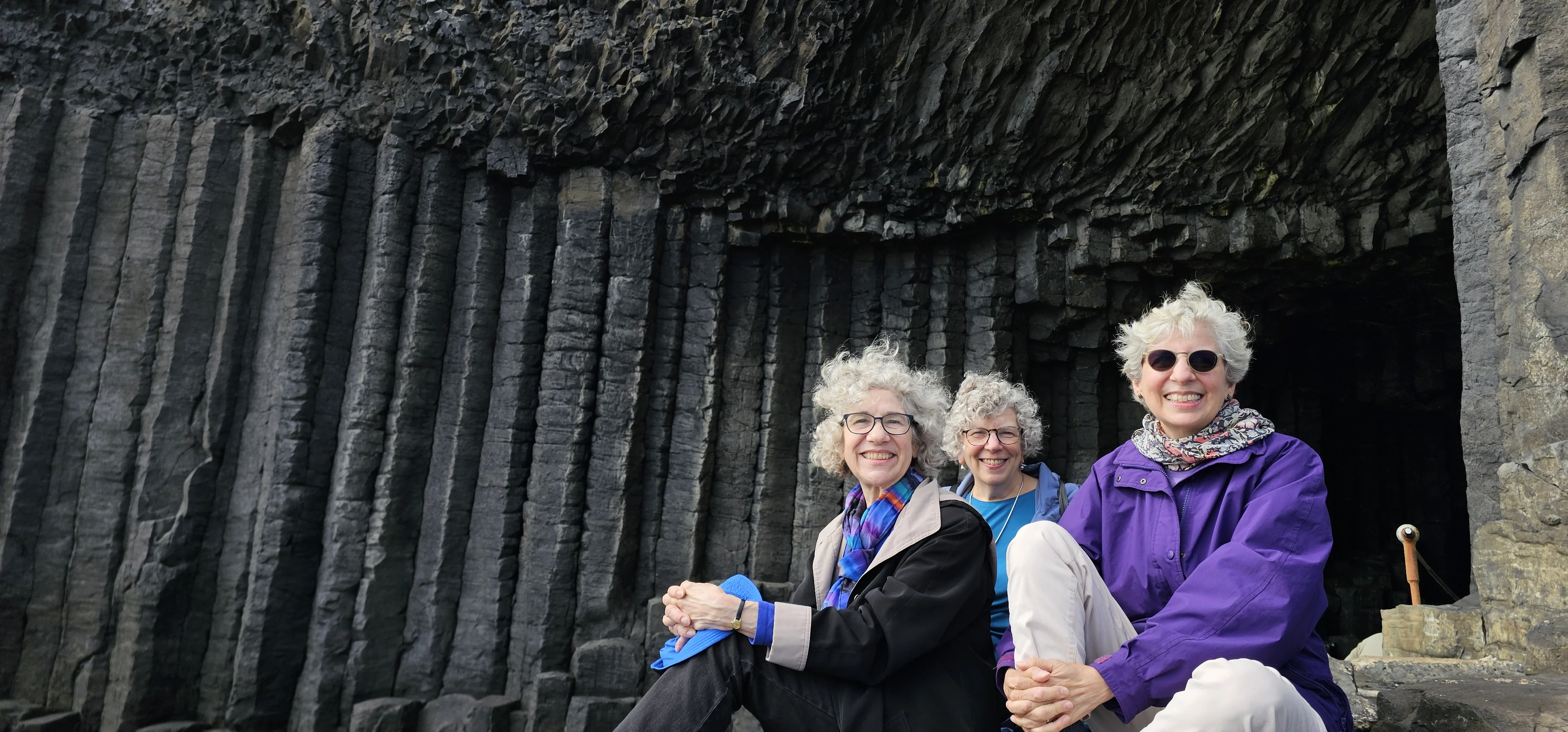 Three women posing at Fingal's Cave with basalt columns backdrop