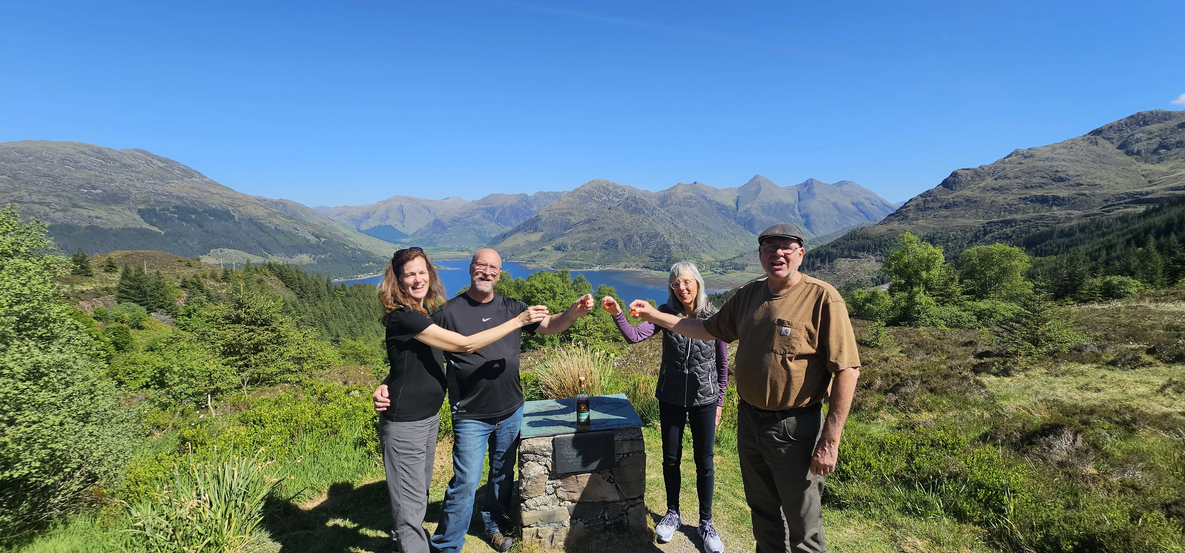 Group of four people posing at Highland viewpoint overlooking mountains and loch