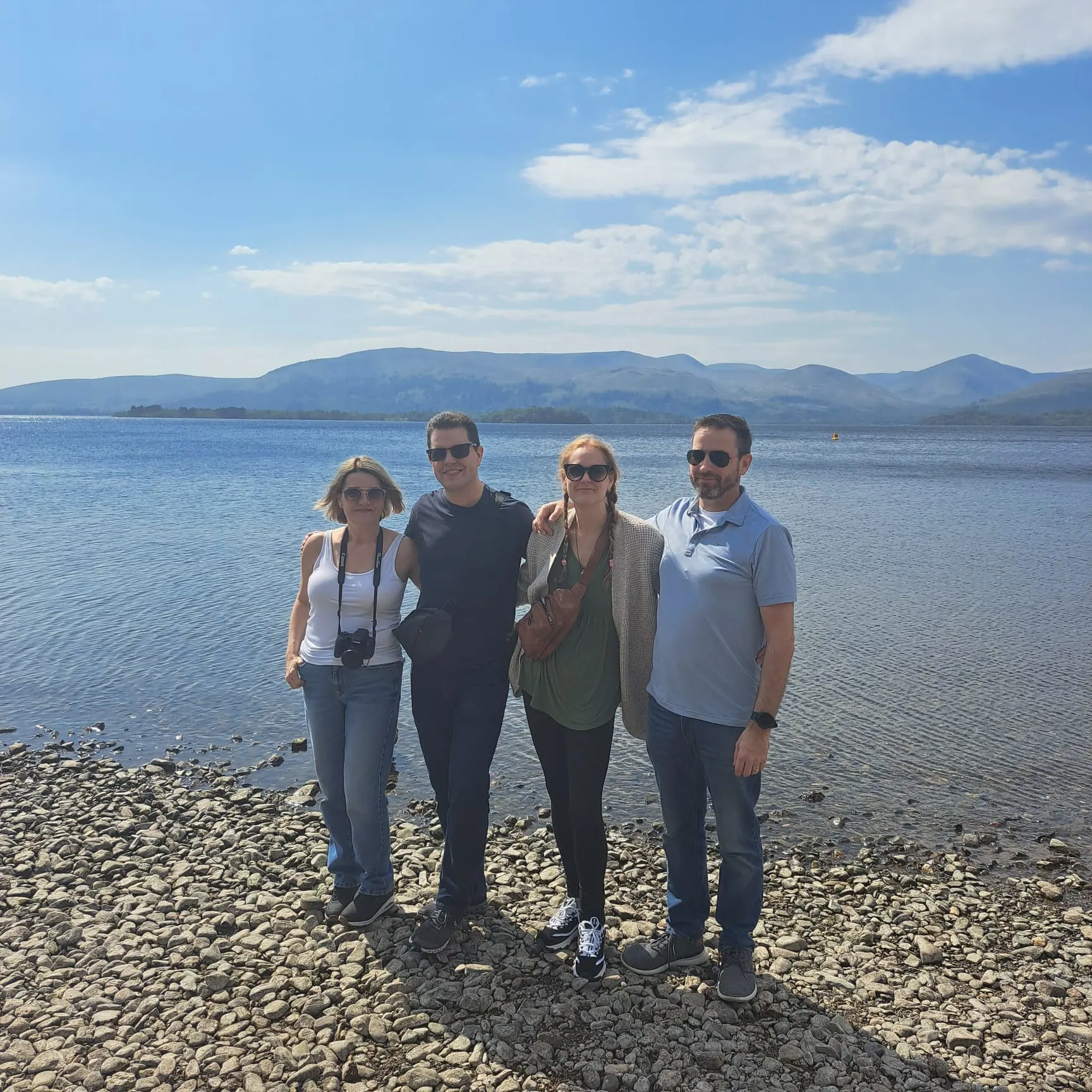 Four tourists pose on Scottish beach with mountains across the water