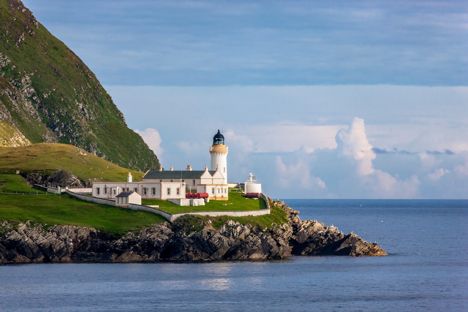 A white lighthouse on a rocky headland in Shetland