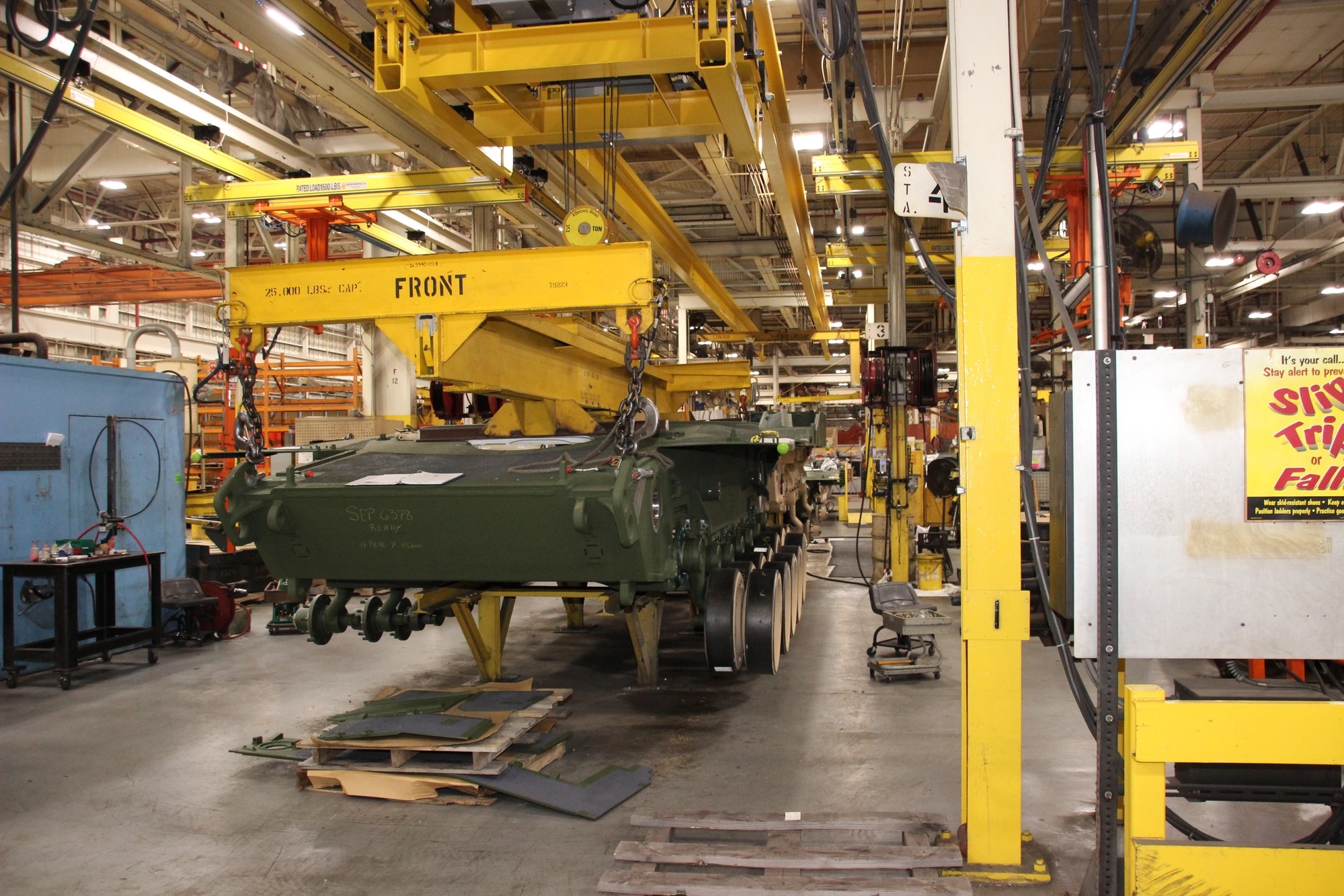 An M1 Abrams hull under overhead gantry cranes on an American manufacturing floor