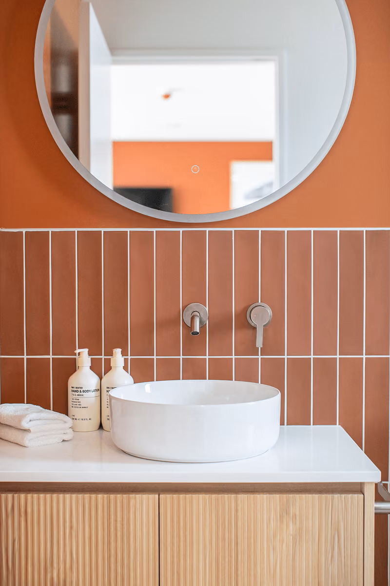 Modern bathroom sink with round white basin, wall-mounted faucet, towels, and bottles on countertop.