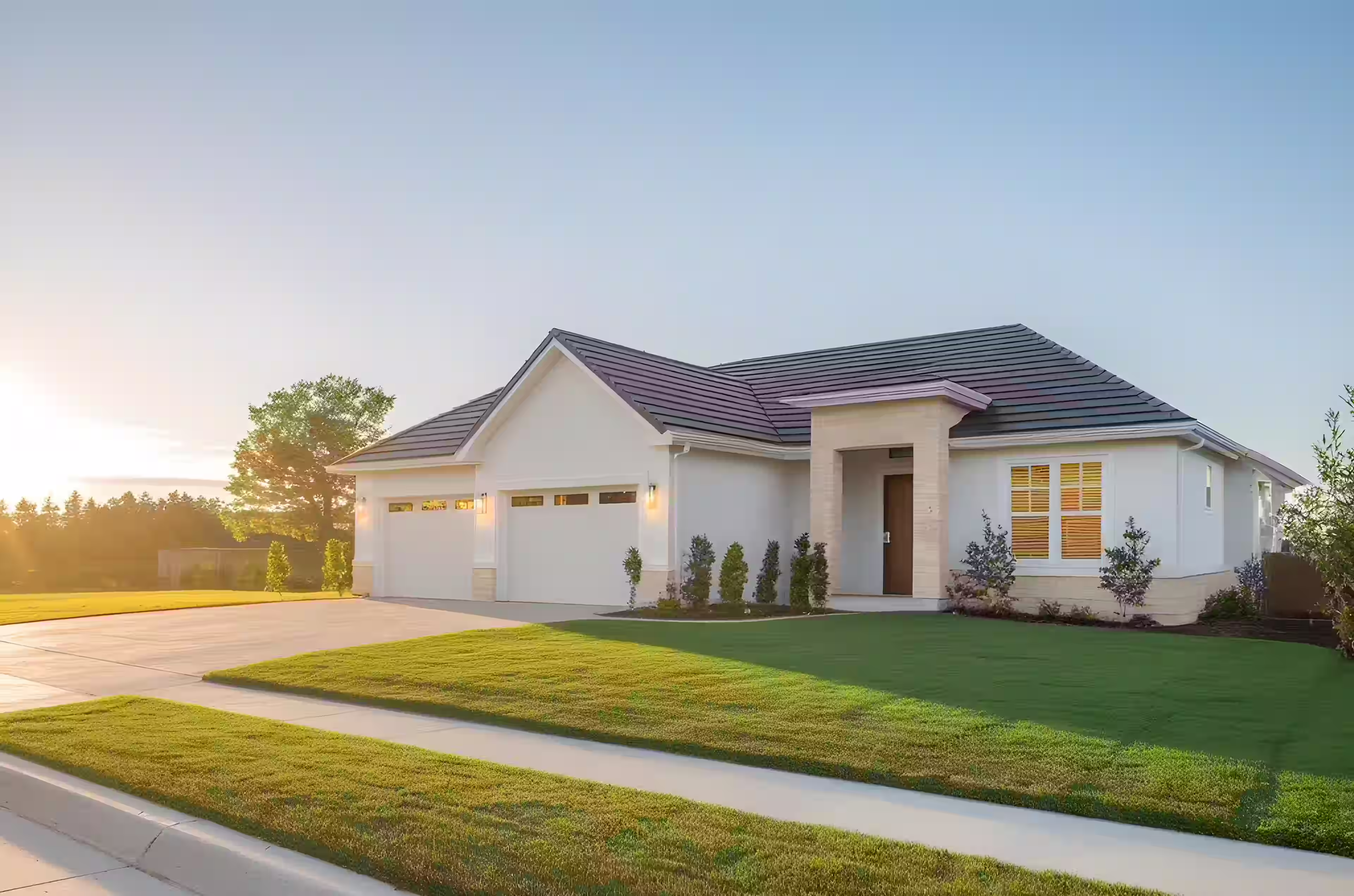 Modern single-story house with a three-car garage and well-maintained green lawn at sunset.