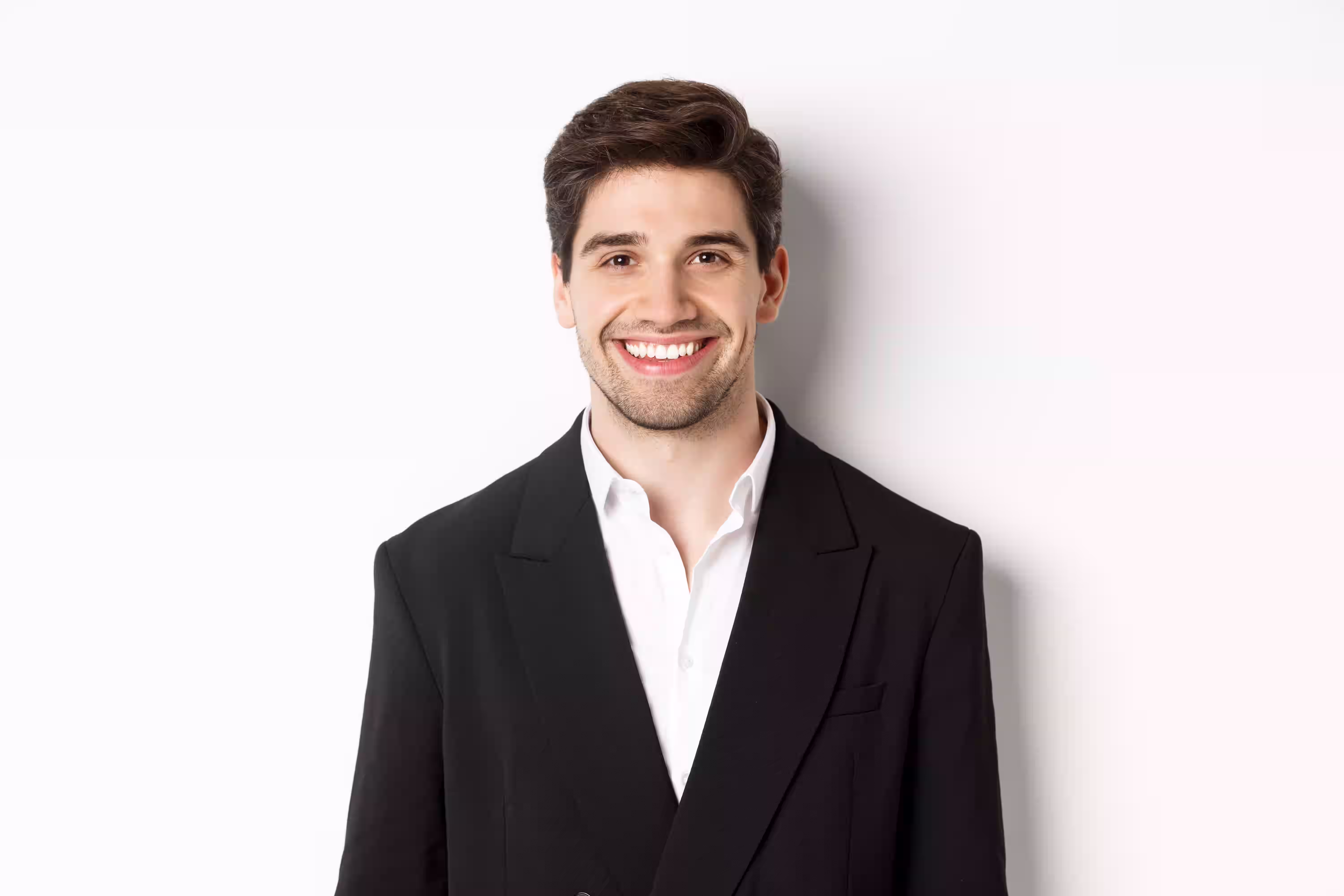 Smiling young man wearing a black suit jacket and white shirt against a white background.