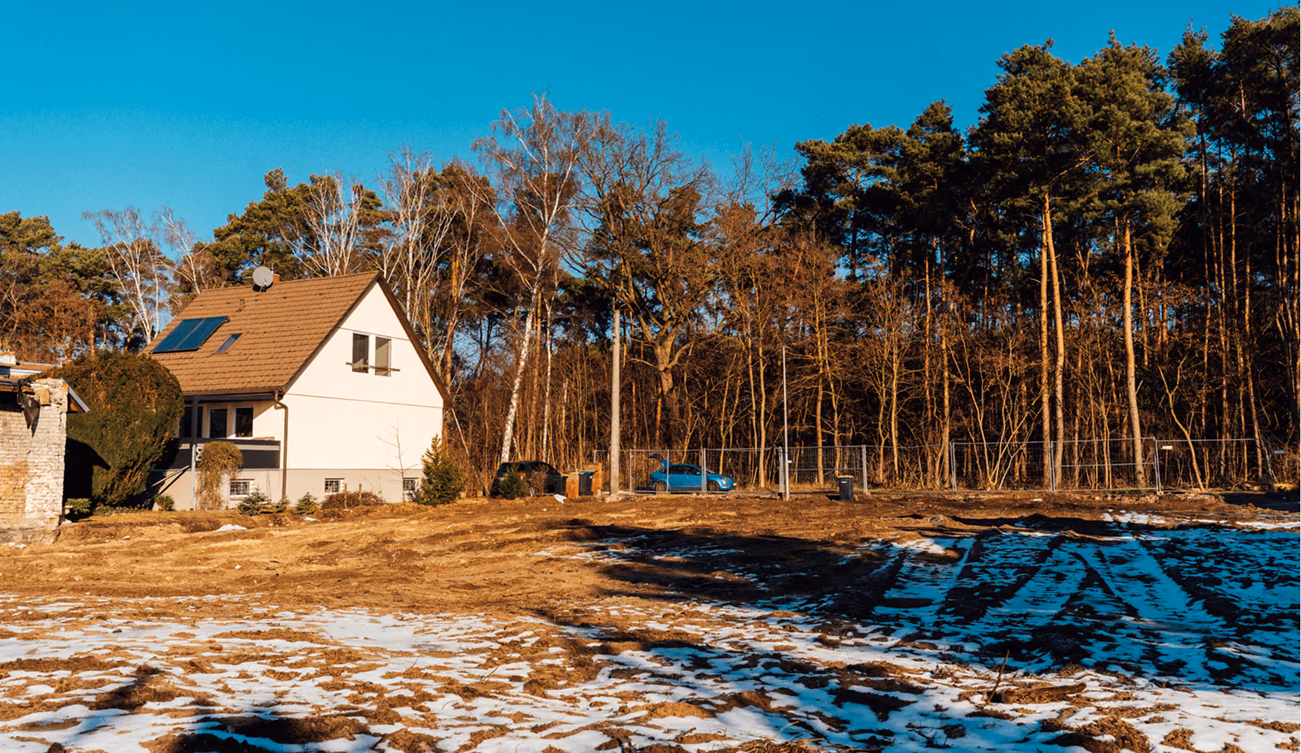 Einfamilienhaus am Waldrand mit schneebedeckter Wiese unter blauem Himmel.