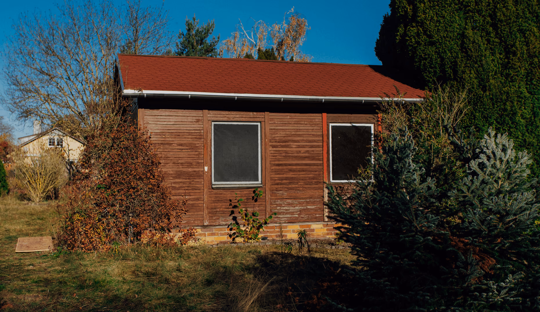 Holzhütte mit rotem Dach umgeben von Bäumen und Sträuchern an einem sonnigen Herbsttag.