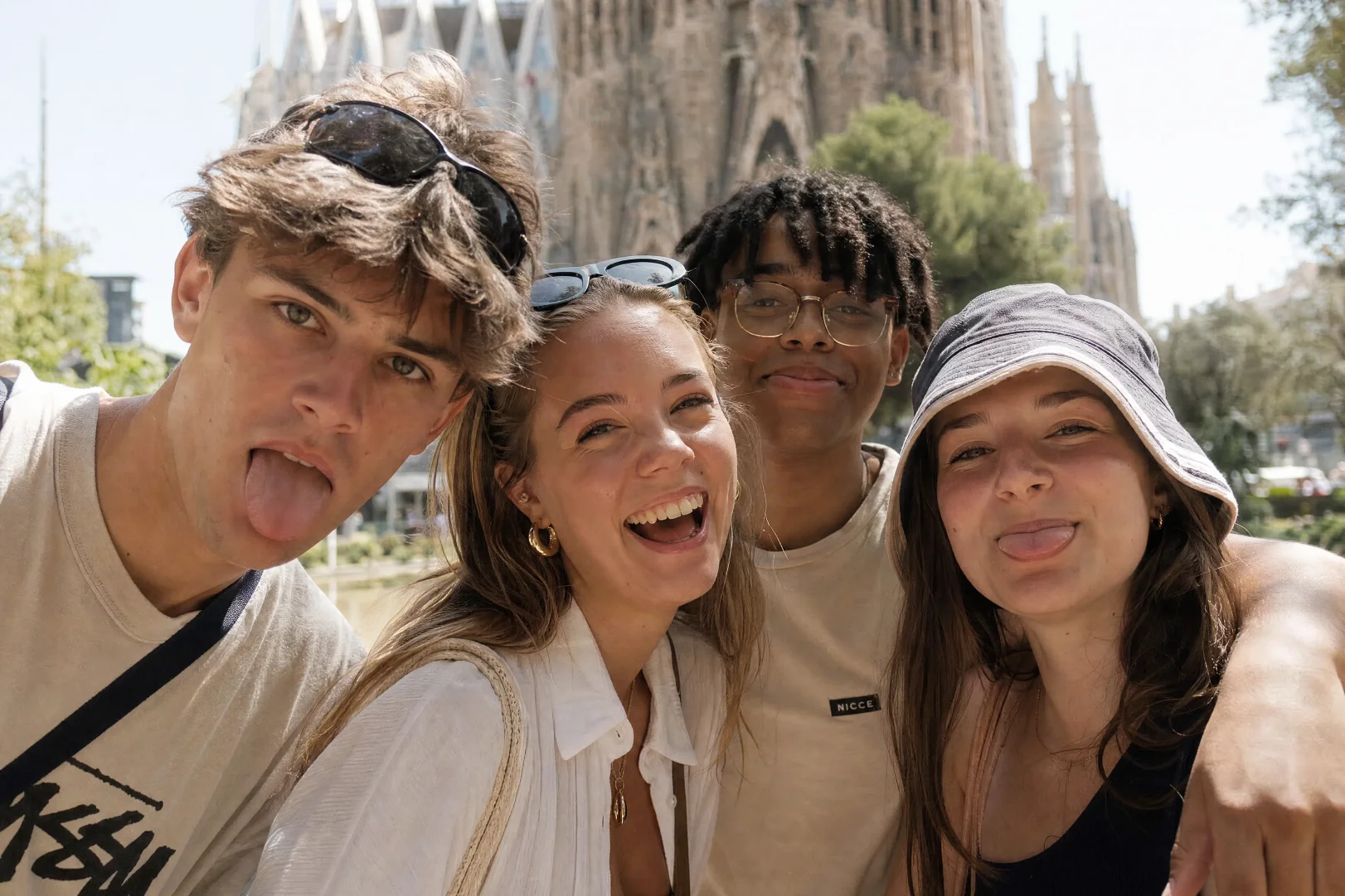 Four young friends smiling and pulling faces for a selfie in front of the Sagrada Familia in Barcelona.