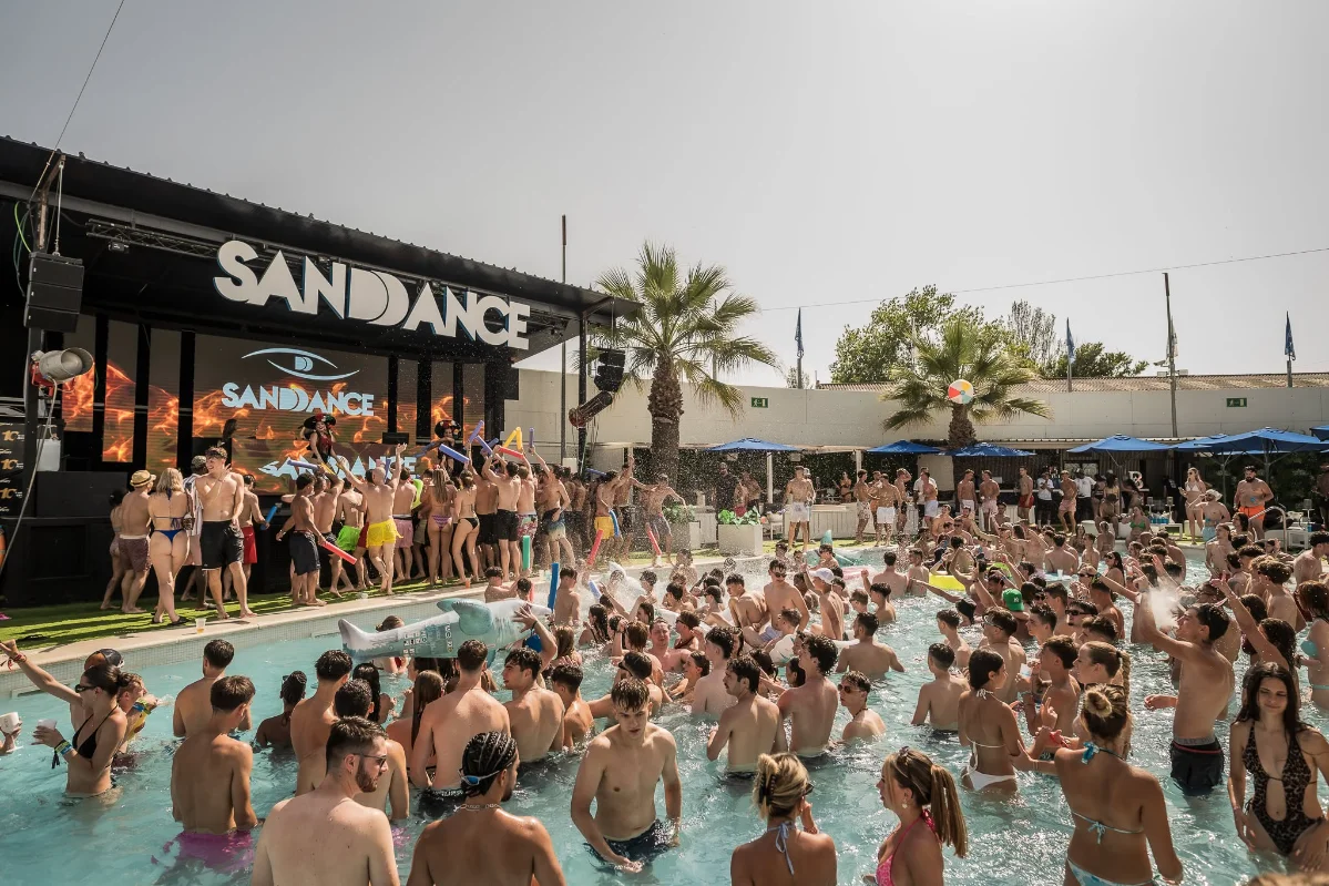 Group enjoying a pool party with sand and dancing at a festival event.