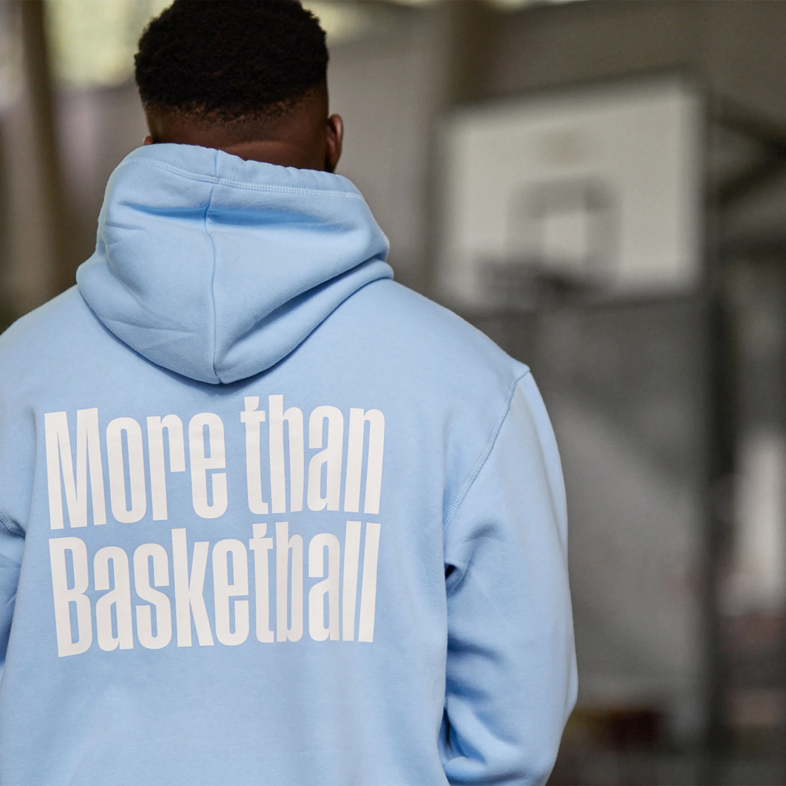 Junger Mann mit hellblauem Hoodie auf dem "more than basketball" steht.