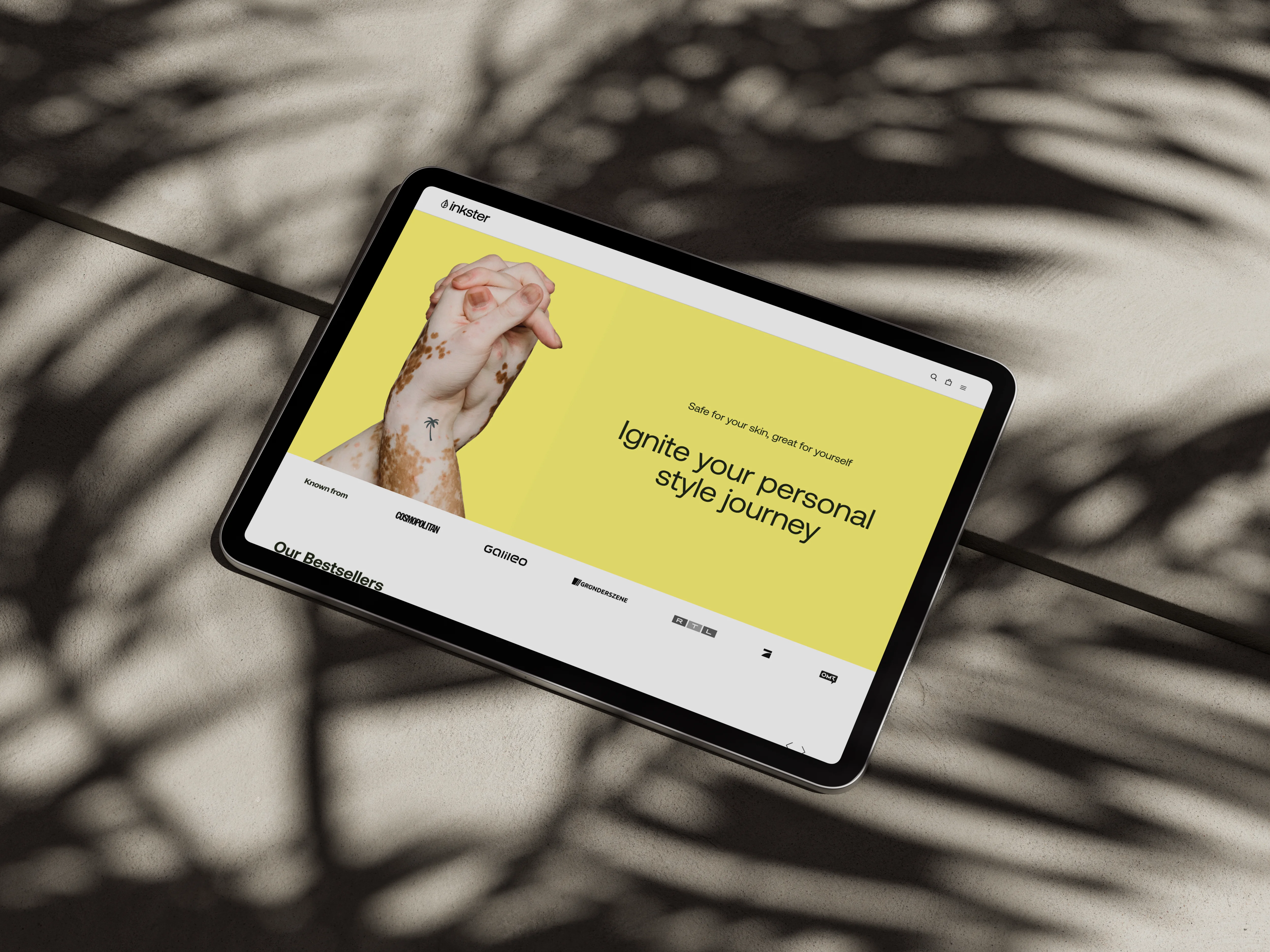 Ein iPad liegt auf einem Steinboden, der Schatten einer Palme liegt quer über dem Bild. Der Bildschirm zeigt die Landing Page der Inkster-Website.