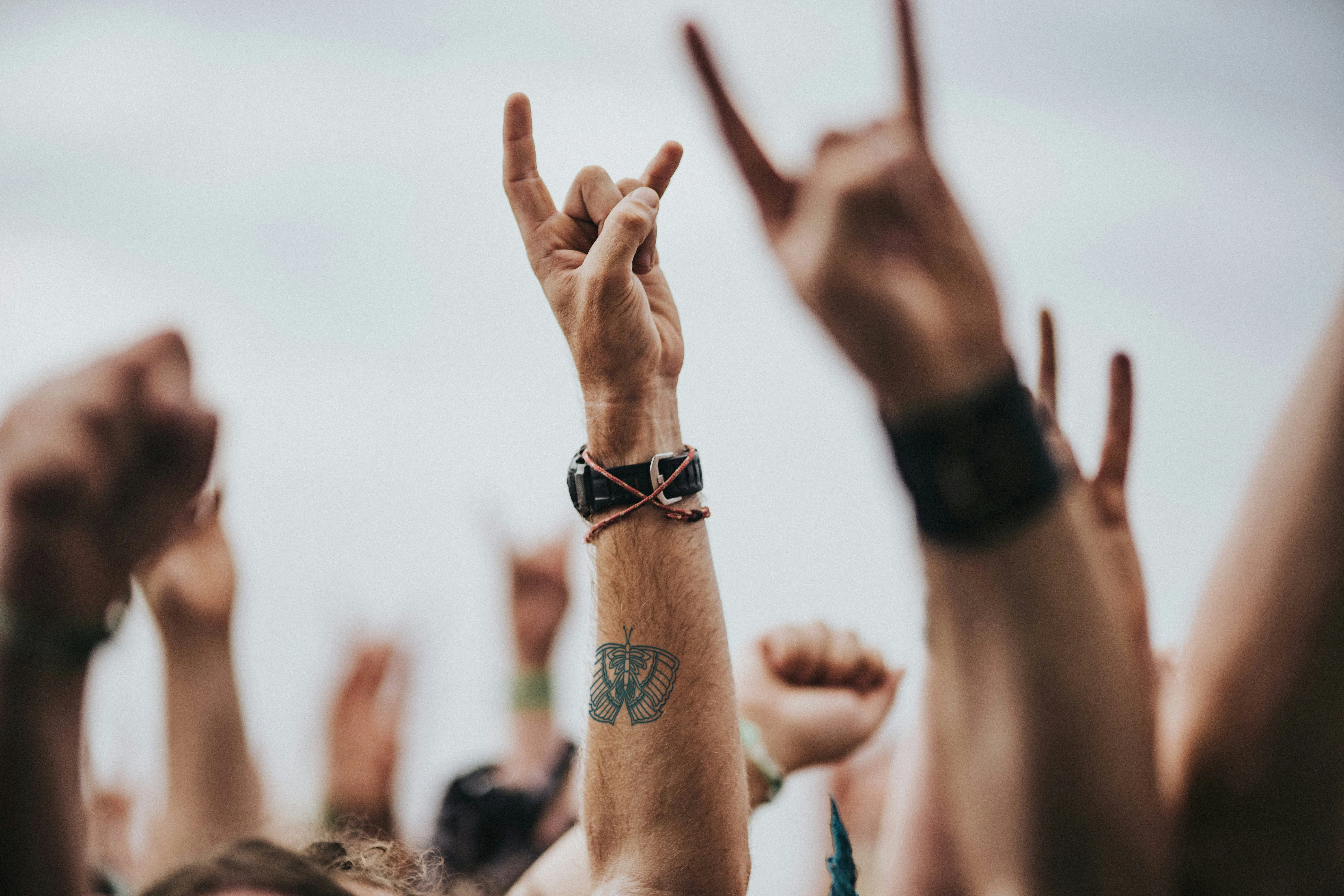 Eine Gruppe von Armen bei einem Konzert. Auf einem der Arme ist die Tätowierung einer Motte zu sehen.