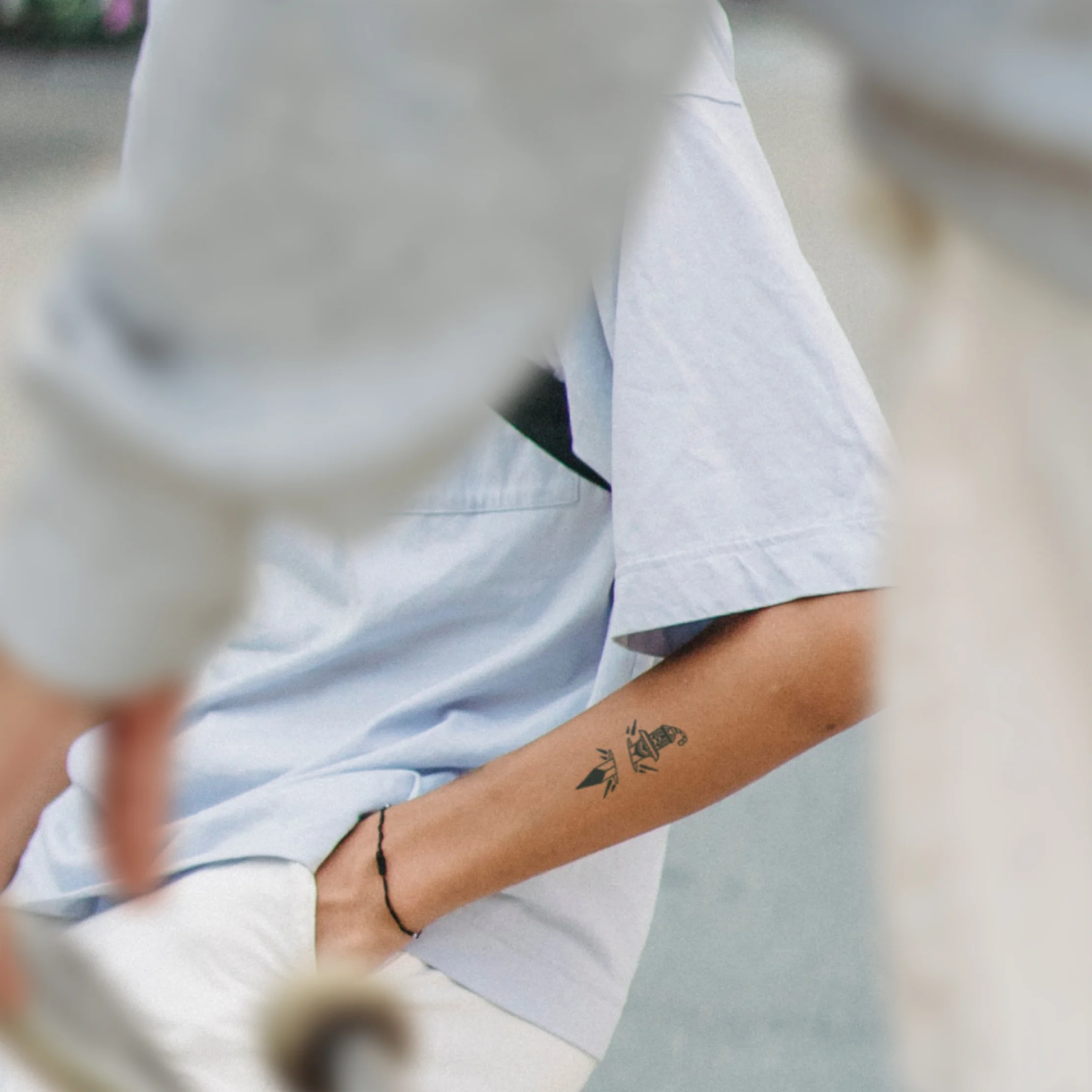Eine Aufnahme zweier Personen. Die hintere Person trägt ein Schwert-Tattoo auf dem Oberarm und hat die Hand in die Hosentasche gesteckt.