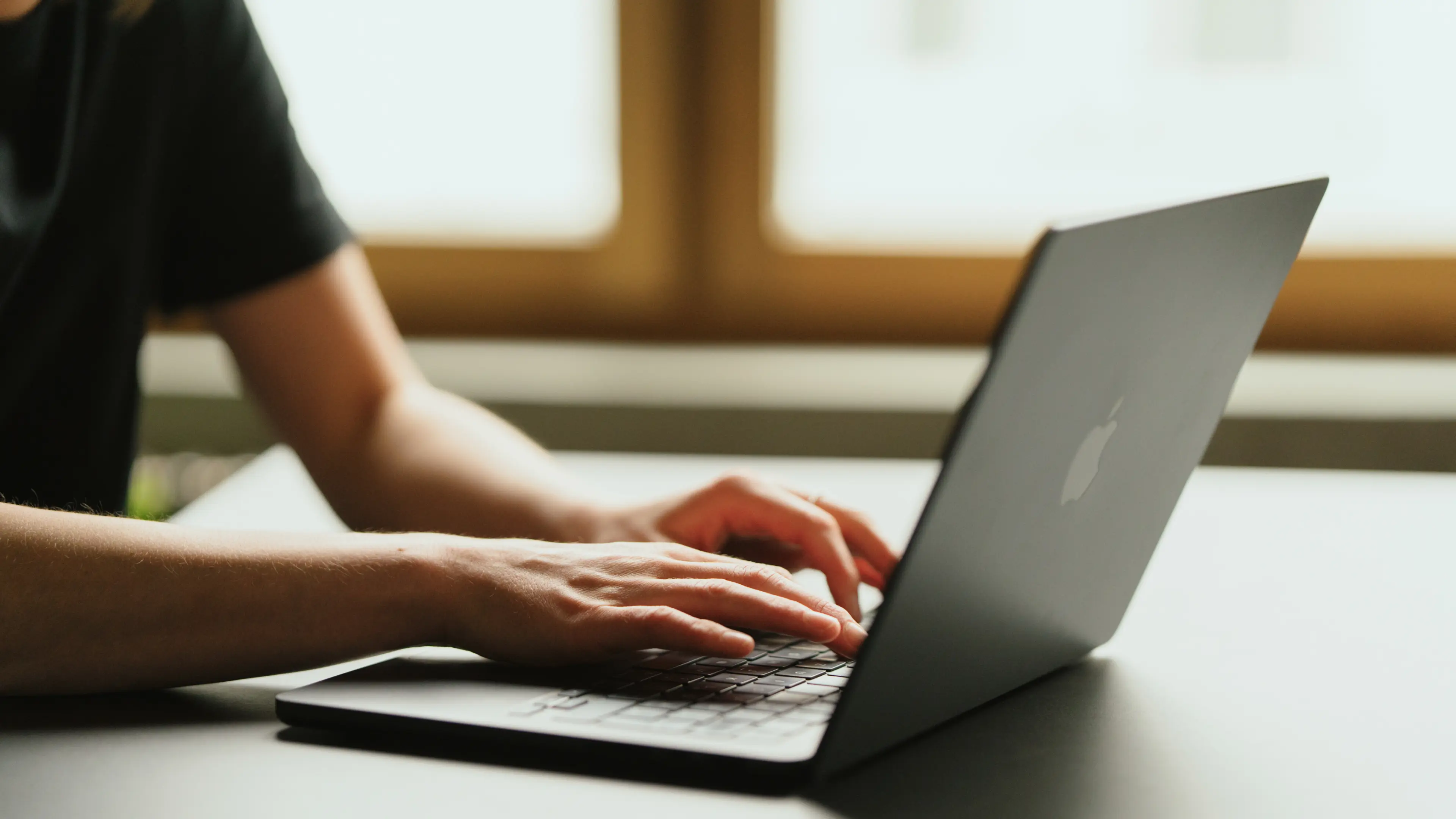 Eine Person tippt auf einem schwarzen Laptop in der Nähe eines Fensters.