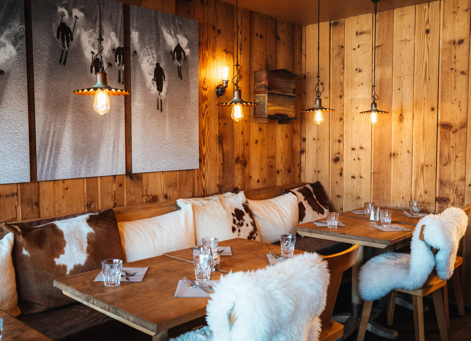 Coin repas chaleureux en bois, avec des chaises recouvertes de fourrure, des coussins en peau de veau et des suspensions, restaurant La Brasserie à Avoriaz, Haute-Savoie, France.