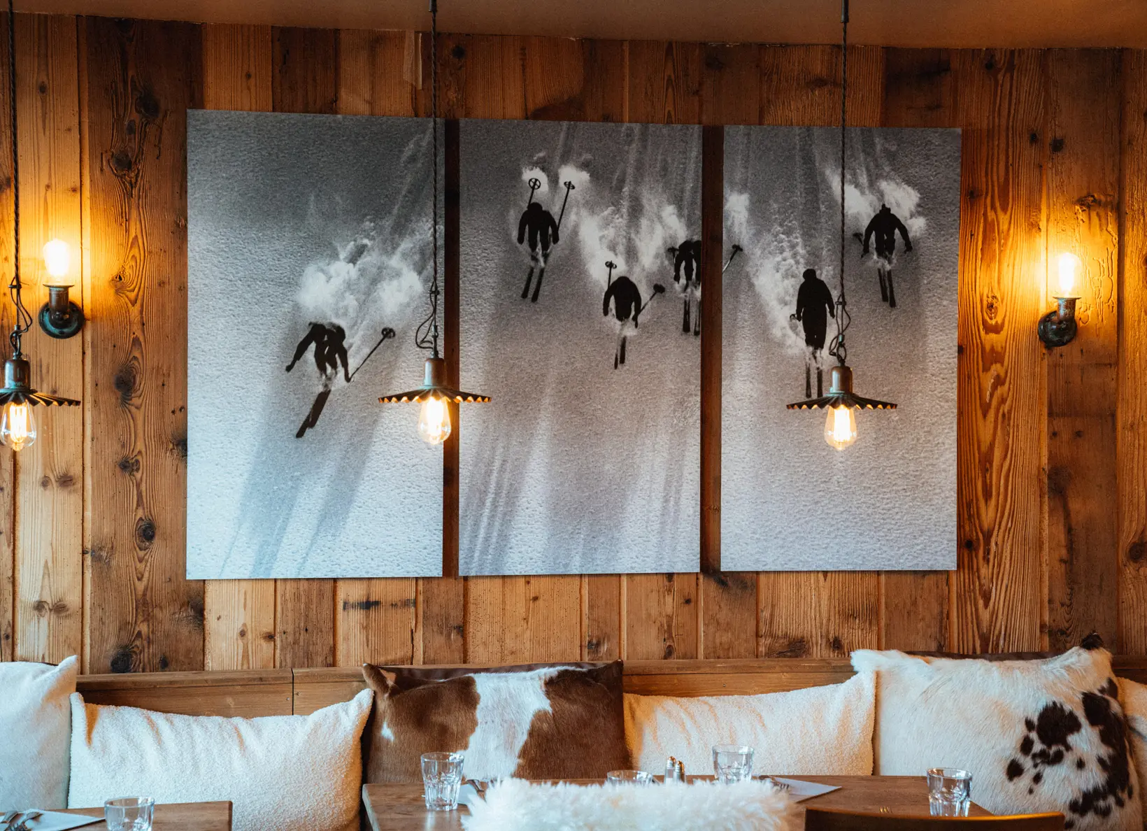 Coin repas rustique avec des coussins en peau de vache, des murs en bois et des photos de ski en noir et blanc aux murs, restaurant La Brasserie à Avoriaz, Haute-Savoie, France.