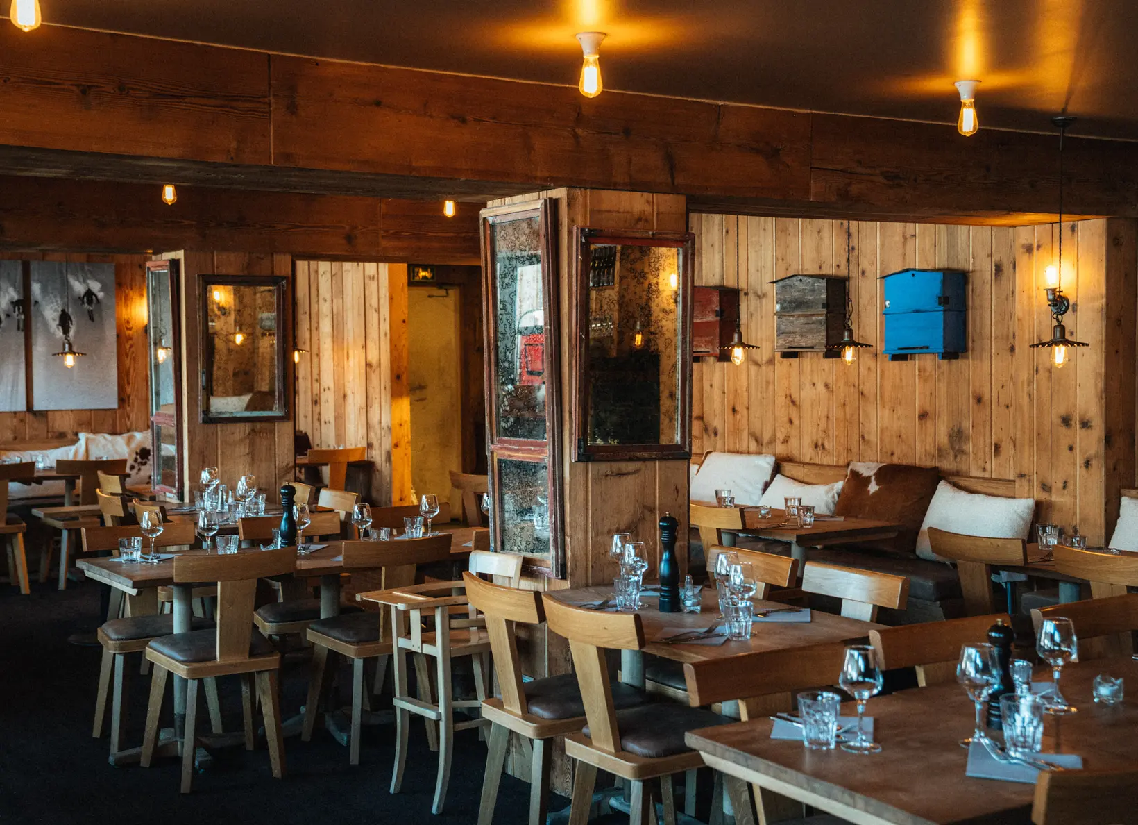 Intérieur chaleureux en bois d'un restaurant, avec tables, chaises, coussins et luminaires suspendus à la lumière douce, restaurant La Brasserie à Avoriaz, Haute-Savoie, France.
