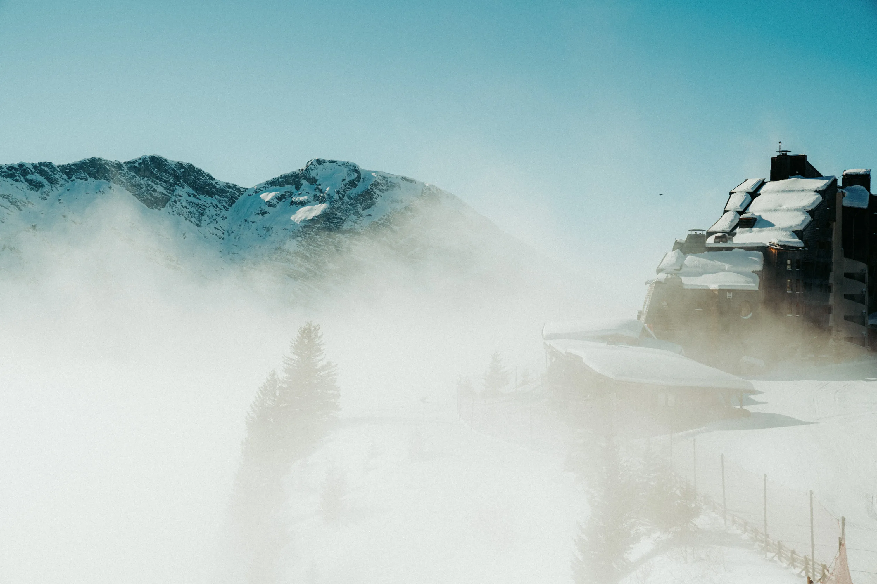 Refuge de montagne enneigé partiellement masqué par le brouillard, avec des pins et des sommets rocheux en arrière-plan, restaurant La Brasserie à Avoriaz, Haute-Savoie, France.
