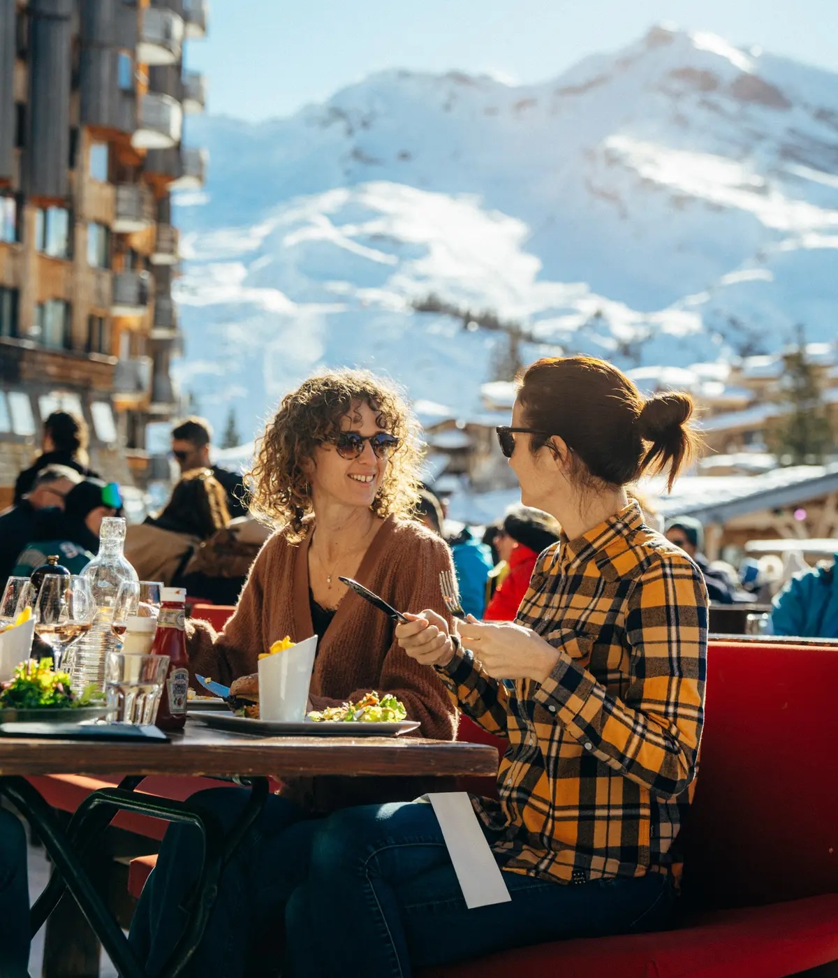 Deux femmes portant des lunettes de soleil dînent en plein air, avec des montagnes enneigées en arrière-plan, restaurant La Brasserie à Avoriaz, Haute-Savoie, France.