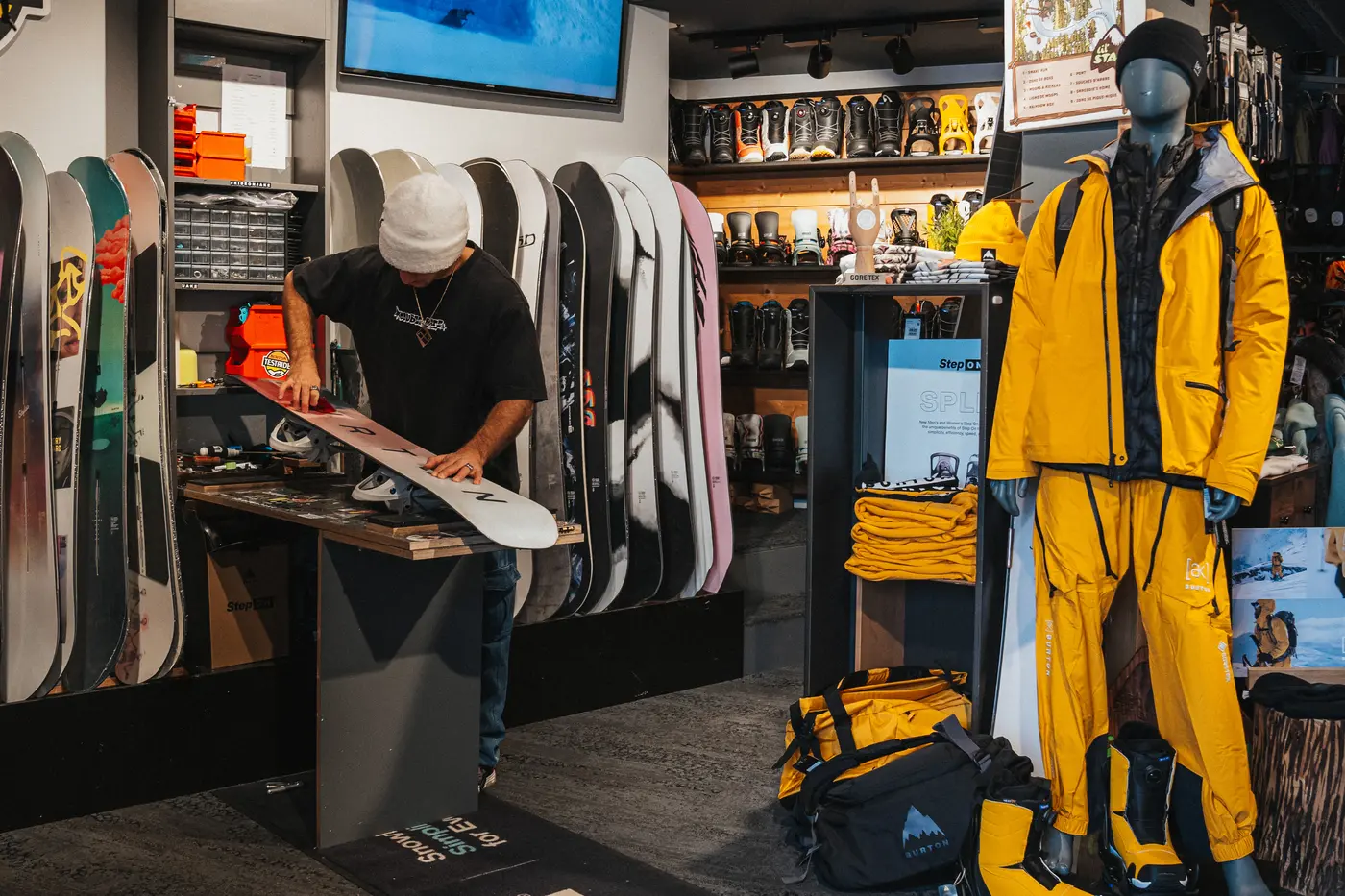 Un homme farte un snowboard dans un magasin doté de présentoirs de snowboards et d'un mannequin vêtu d'une tenue de ski jaune, restaurant La Brasserie à Avoriaz, Haute-Savoie, France.