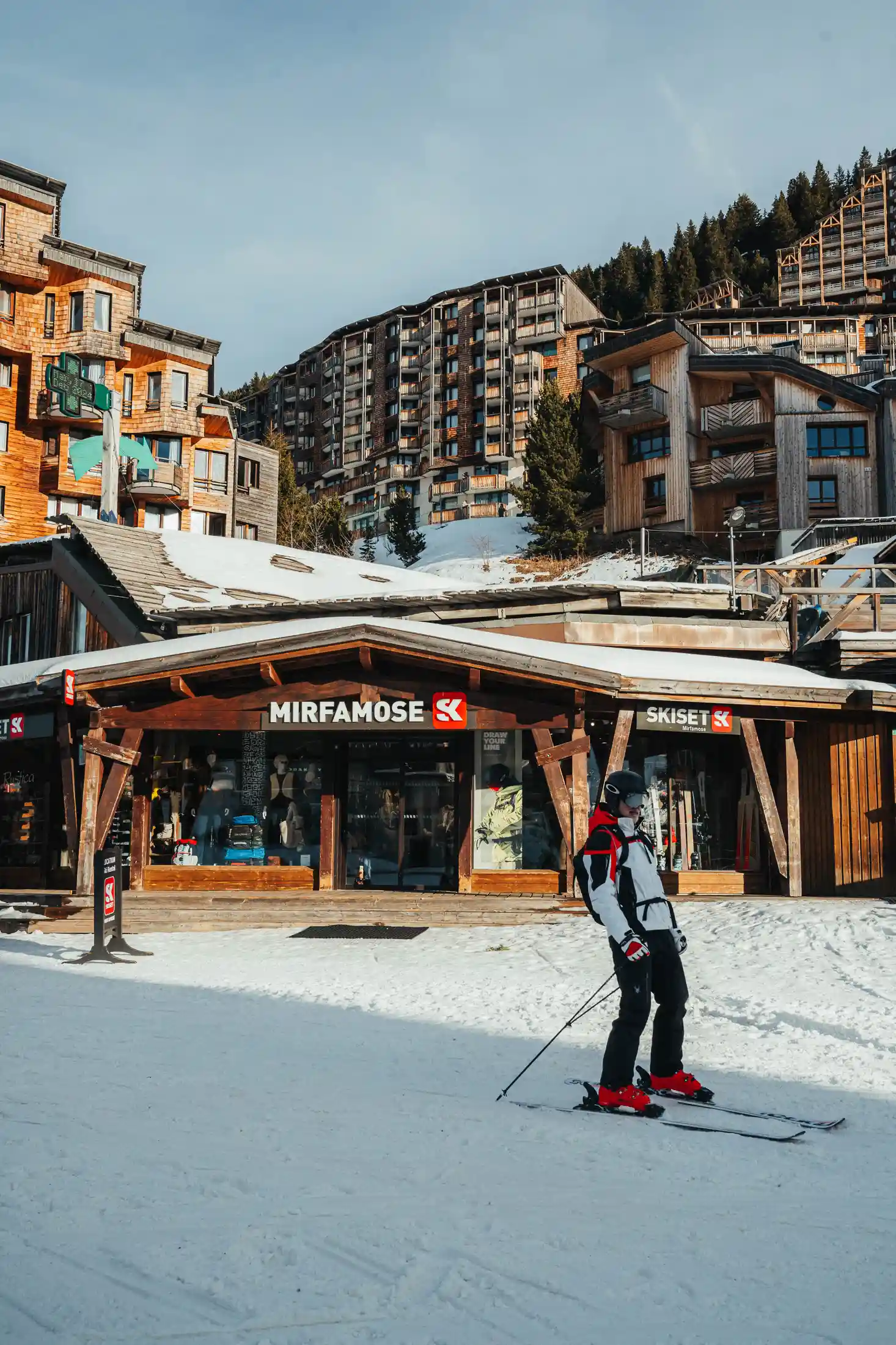 Une personne skie sur la neige devant un magasin de ski en bois nommé Mirfamose, avec des bâtiments de style alpin en arrière-plan, restaurant La Brasserie à Avoriaz, Haute-Savoie, France.