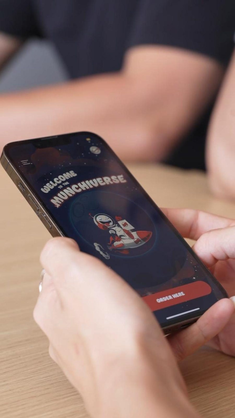 Hands holding a phone showing the Munchiverse app welcome screen
