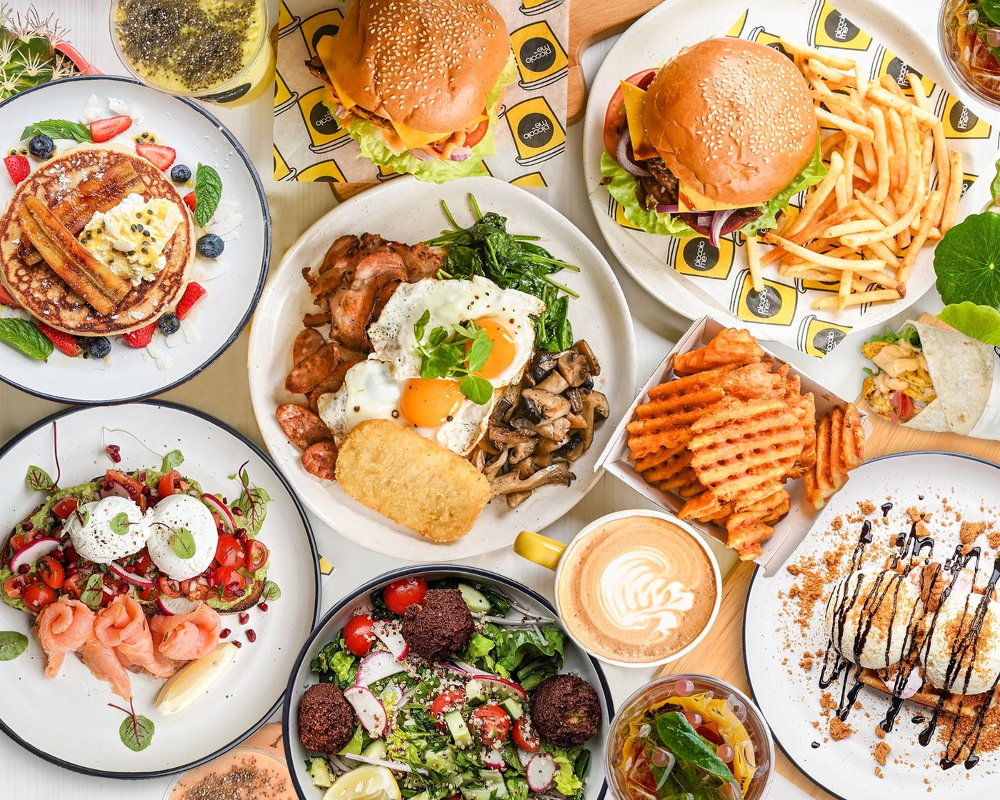 A table of Piccolo Me dishes seen from above: a big breakfast, burgers, pancakes, salads and a coffee