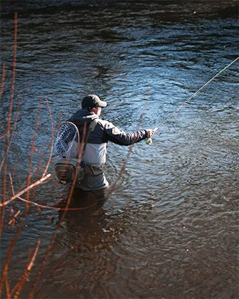 Angler wearing fishing gear standing in a river casting a fishing line.