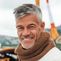 Smiling mature man with gray hair wearing a brown scarf and white jacket outdoors.