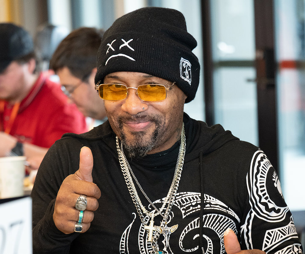Man wearing a black beanie and yellow glasses giving a thumbs-up while smiling.