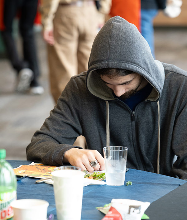 Person in gray hoodie looking down at a plate of food on a blue tablecloth with drinks nearby.