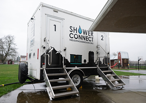 Mobile shower unit with stairs labeled 1 and 2 on wet pavement in an outdoor setting.