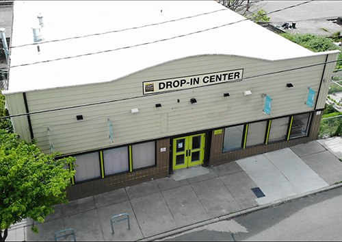Aerial view of a building labeled 'DROP-IN CENTER' with yellow doors on a city street.