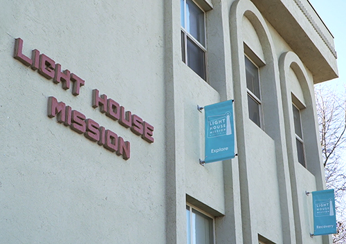 Light House Mission building exterior with signage and blue banners near windows.