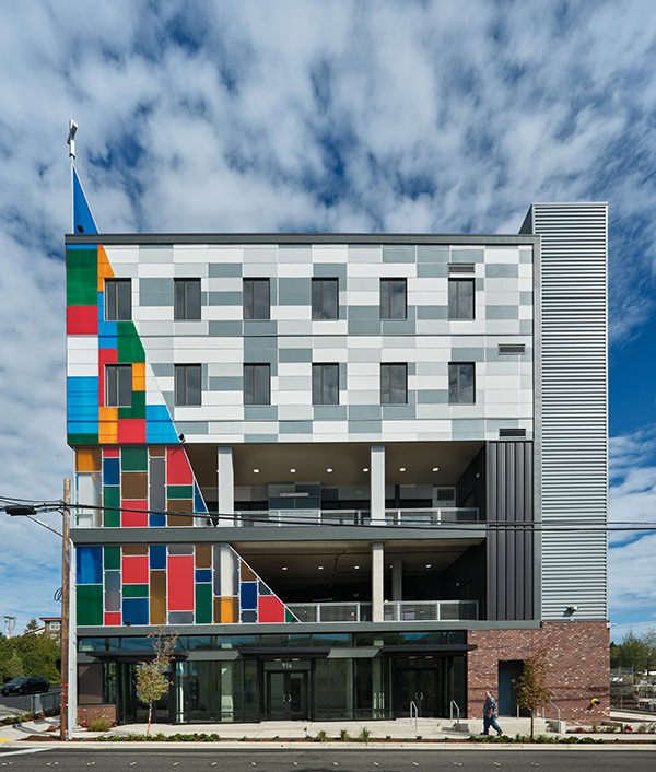 Modern multi-story building with colorful geometric panels on the left and gray facade on the right.