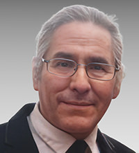 Portrait of Chef Richard Fortune with glasses, gray hair, and a slight smile in a suit and tie.
