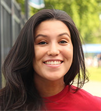 Rebecca Ricks with long dark hair smiling outdoors with green trees in the background.