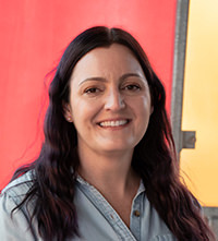 Brittany Hargrove with long dark hair wearing a light blue shirt in front of a red and yellow background.
