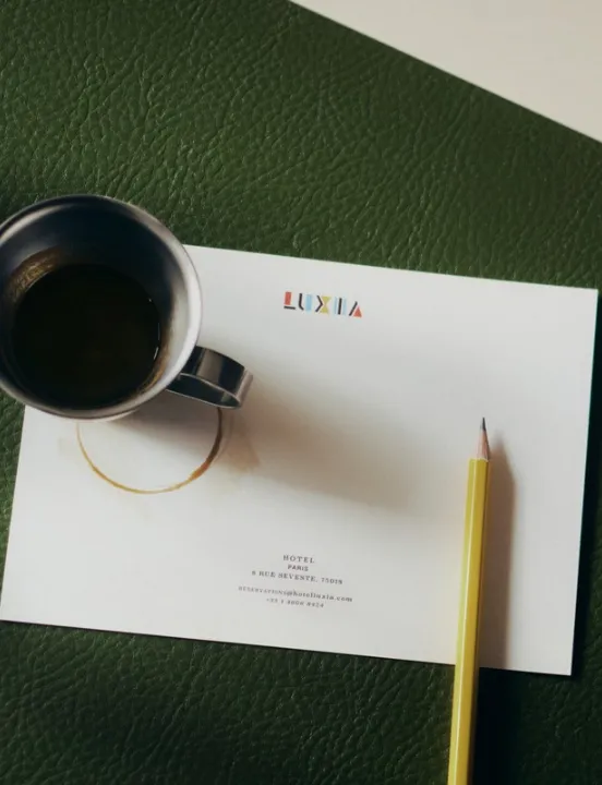 Luxia hotel letterhead resting on a green leather desk pad, with a metal coffee cup and a yellow pencil.
