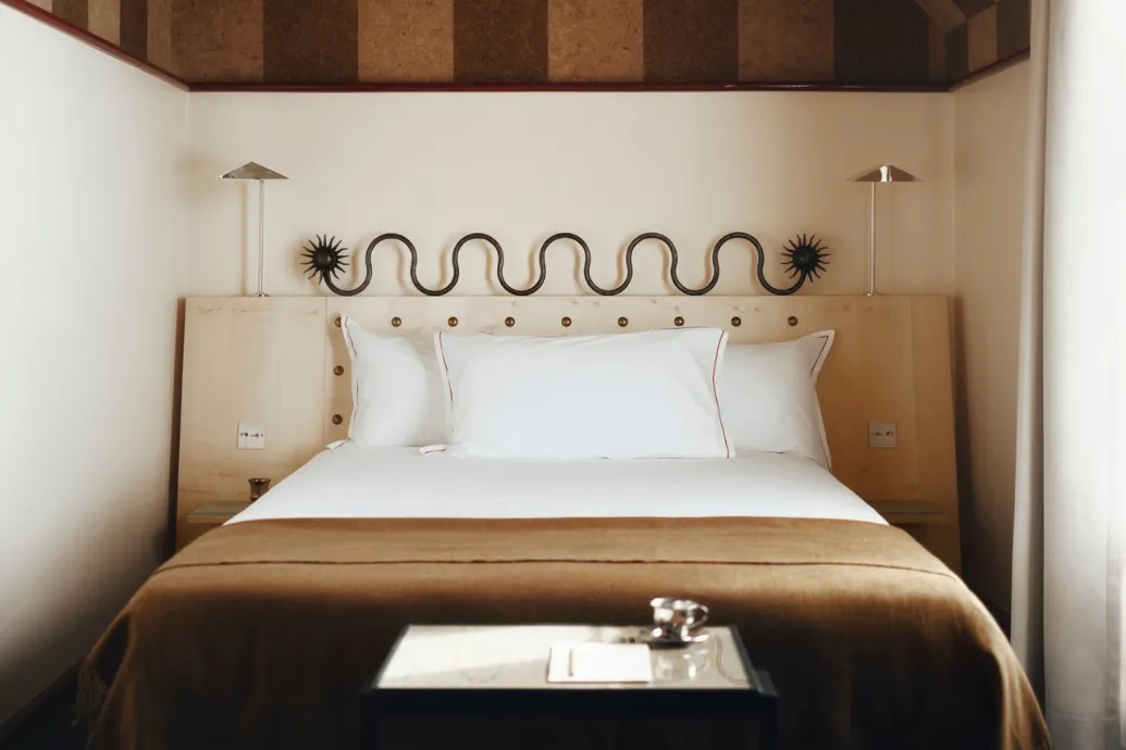 Miniature d'une chambre avec un lit au jeté marron, une tête de lit en bois et un motif ondulé noir au-dessus des oreillers.