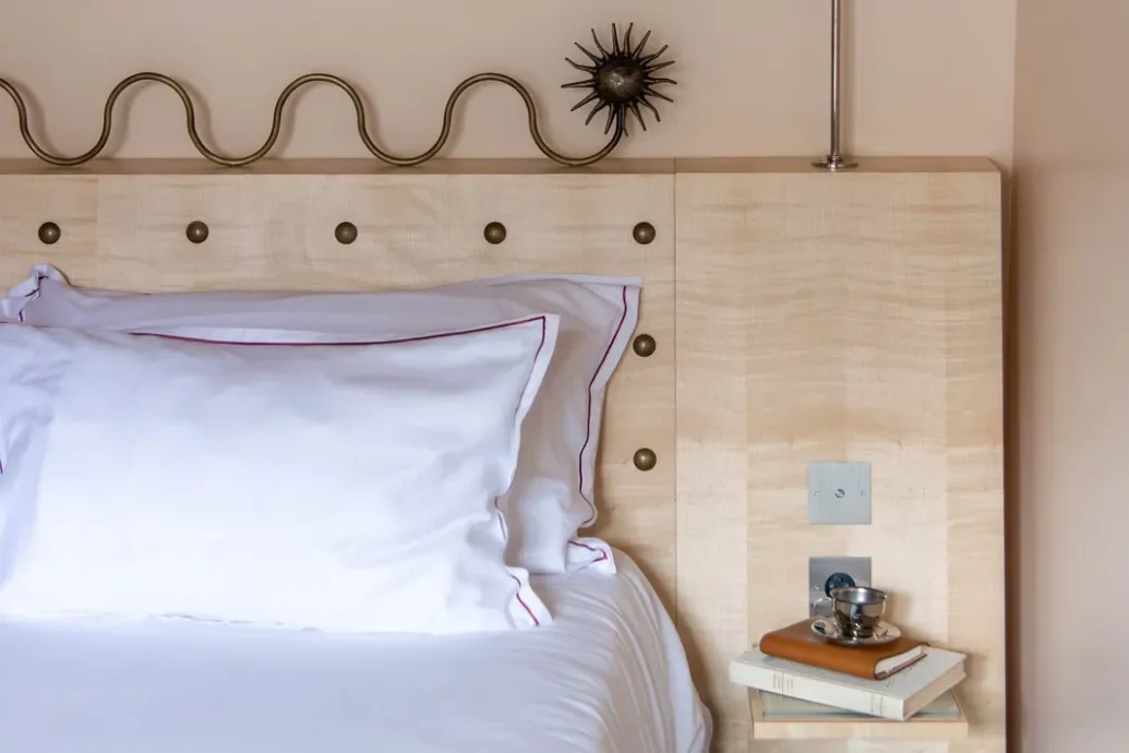 Vignette d'un lit aux oreillers blancs contre une tête de lit en bois clair, avec un livre posé sur le chevet.