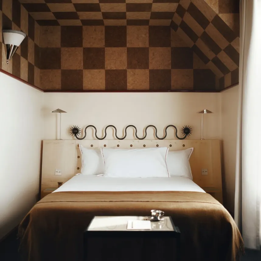 Chambre avec un lit double au plaid camel, une tête de lit en bois ornée d'une sculpture ondulée et un plafond en liège à damier.