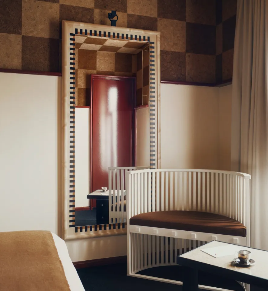 Détail déco d'une chambre associant un siège arrondi laqué blanc, une table basse avec tasse en argent et un miroir rectangulaire bordé de carrés noirs.